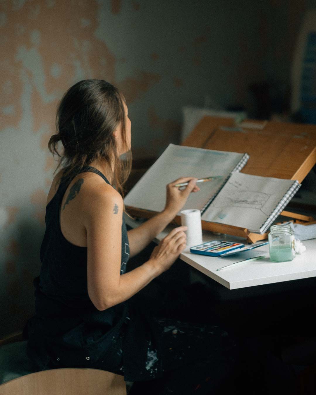 Student studying at wooden desk with notebook and calculator while completing schoolwork in moody lighting.