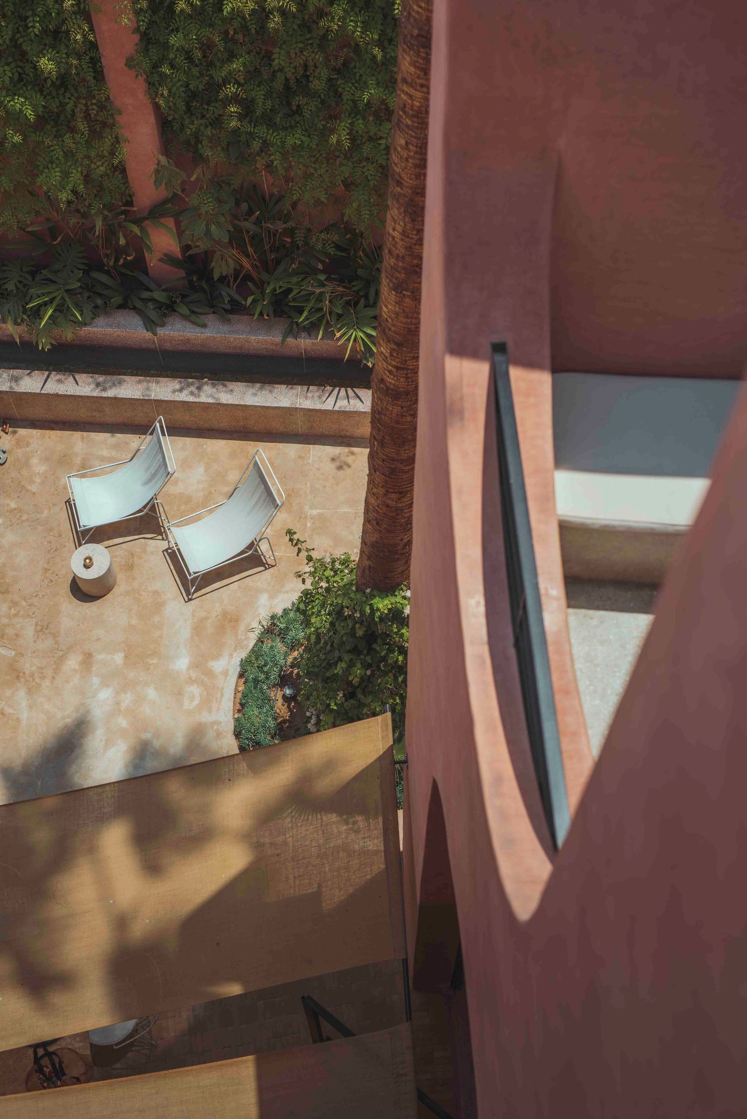 Overhead view of patio loungers and greenery against desert-style architecture with dramatic shadows.