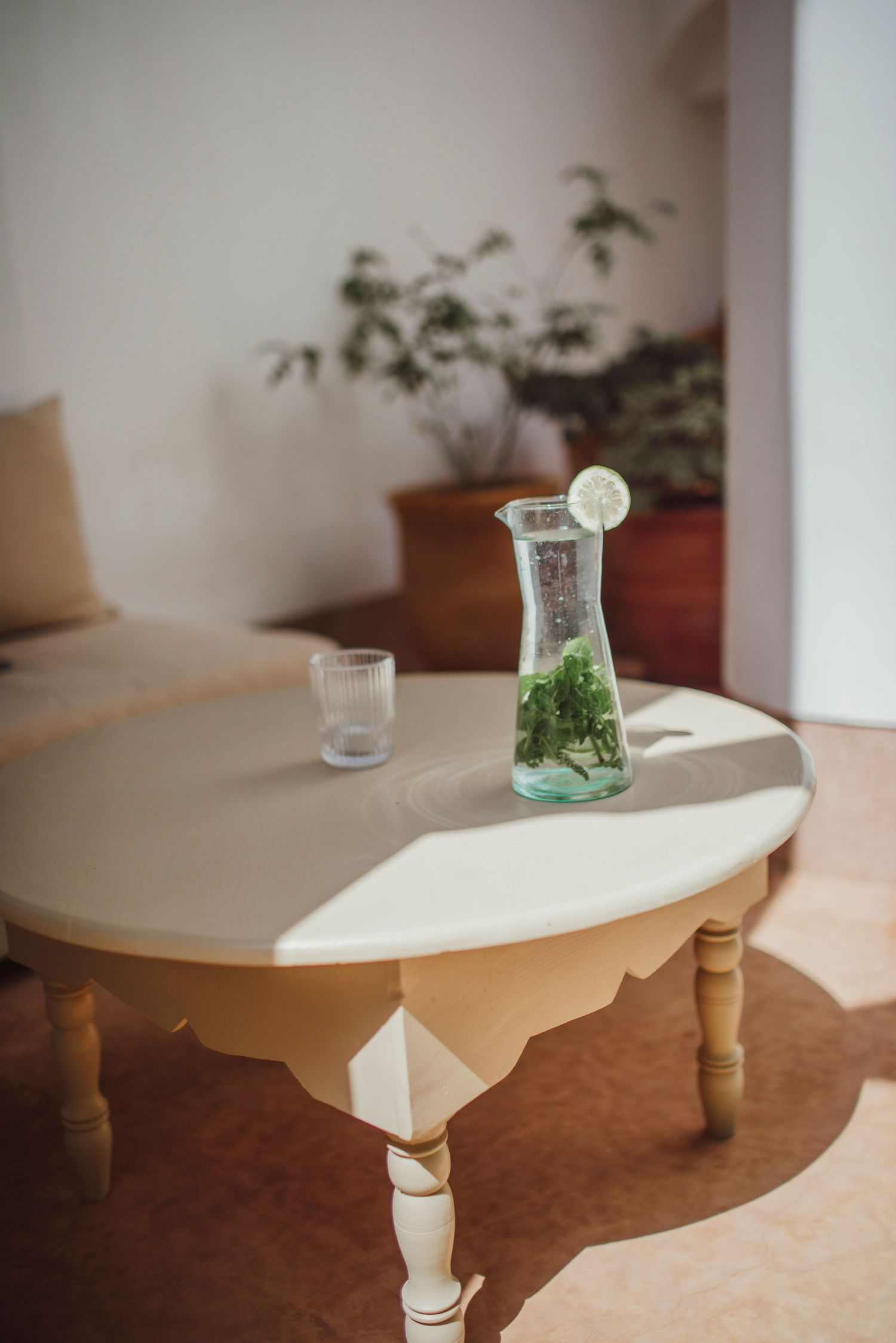 Glass carafe with mint and lemon water on white round table in minimalist setting.