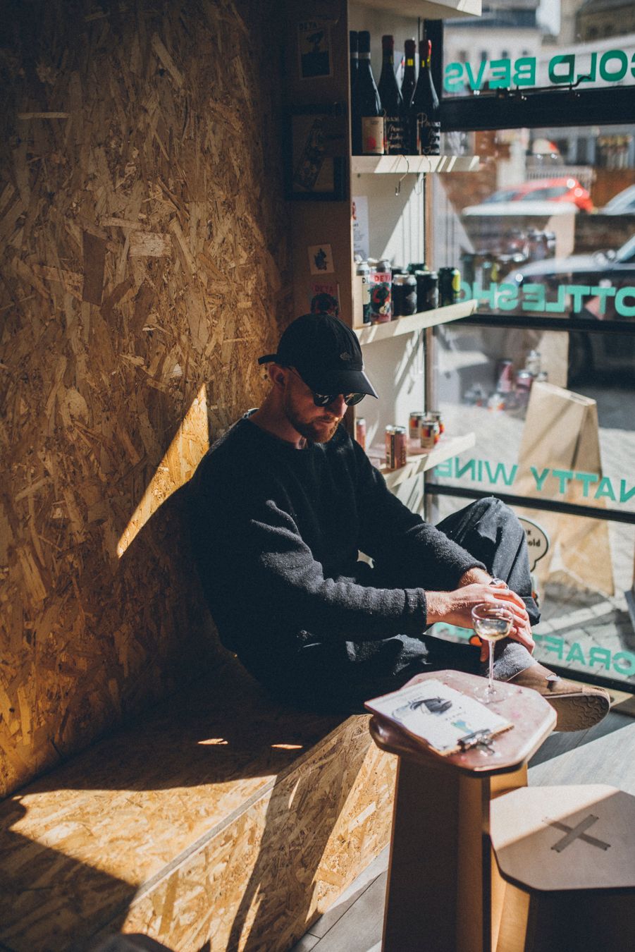 Person in casual attire enjoying wine at a cozy wine shop corner.