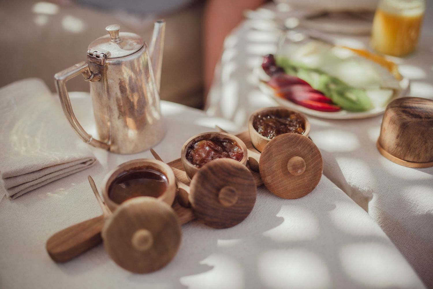 Breakfast table setting with silver teapot and wooden containers for condiments.