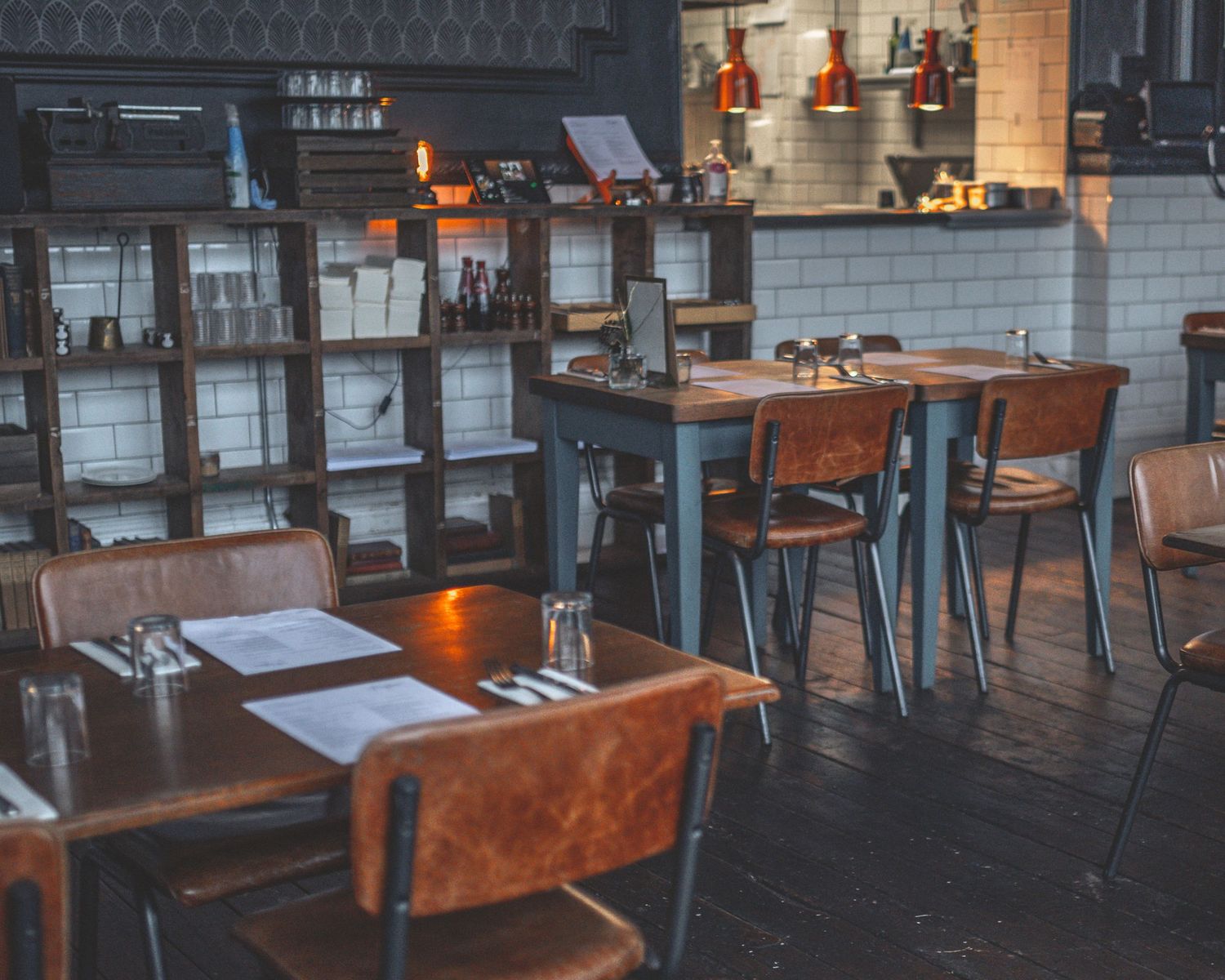 Modern restaurant interior with brown leather seating and wood tables in a cozy industrial setting.