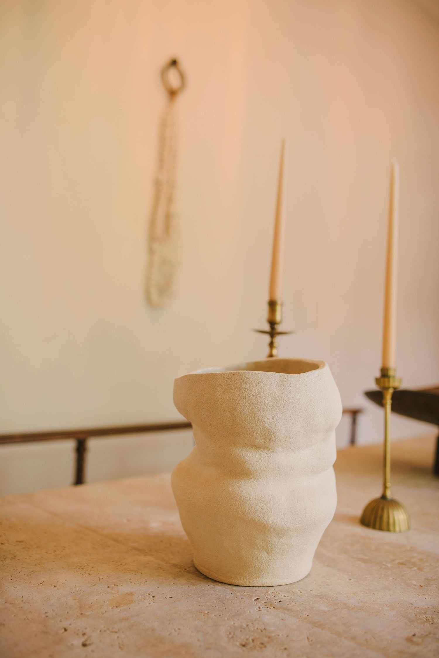 White ceramic vase with curved shape displayed next to brass candlesticks on stone surface.