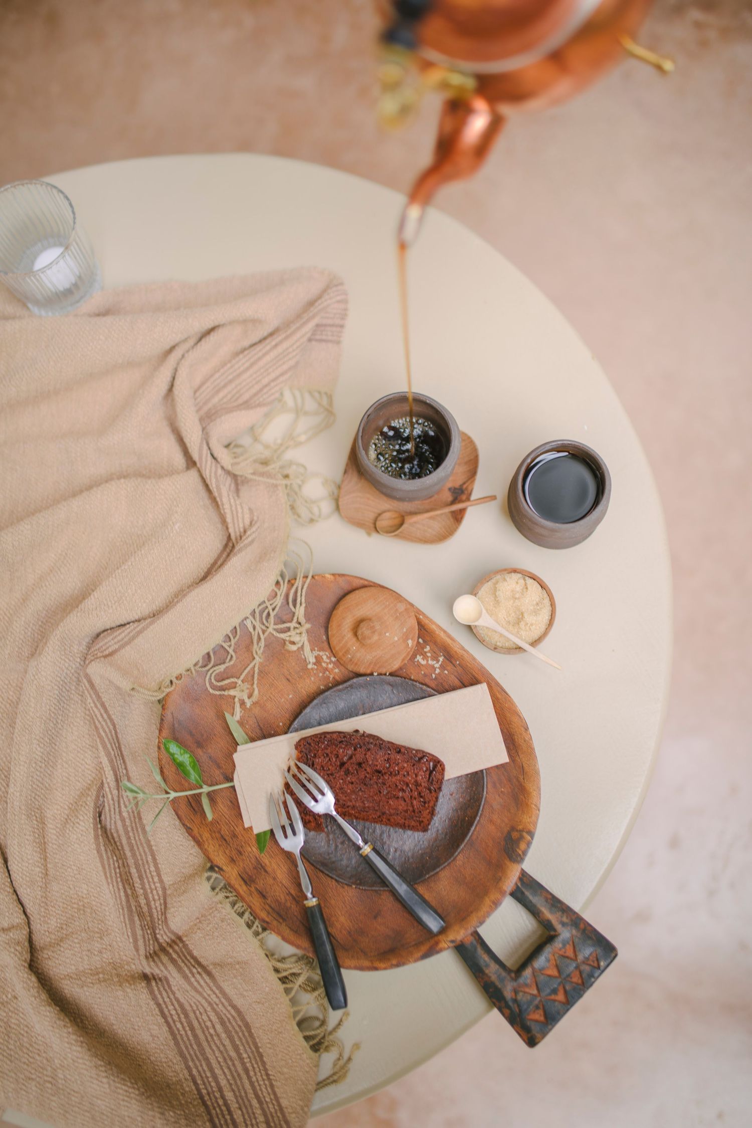 Overhead view of chocolate cake and utensils on terracotta plates with neutral linens.