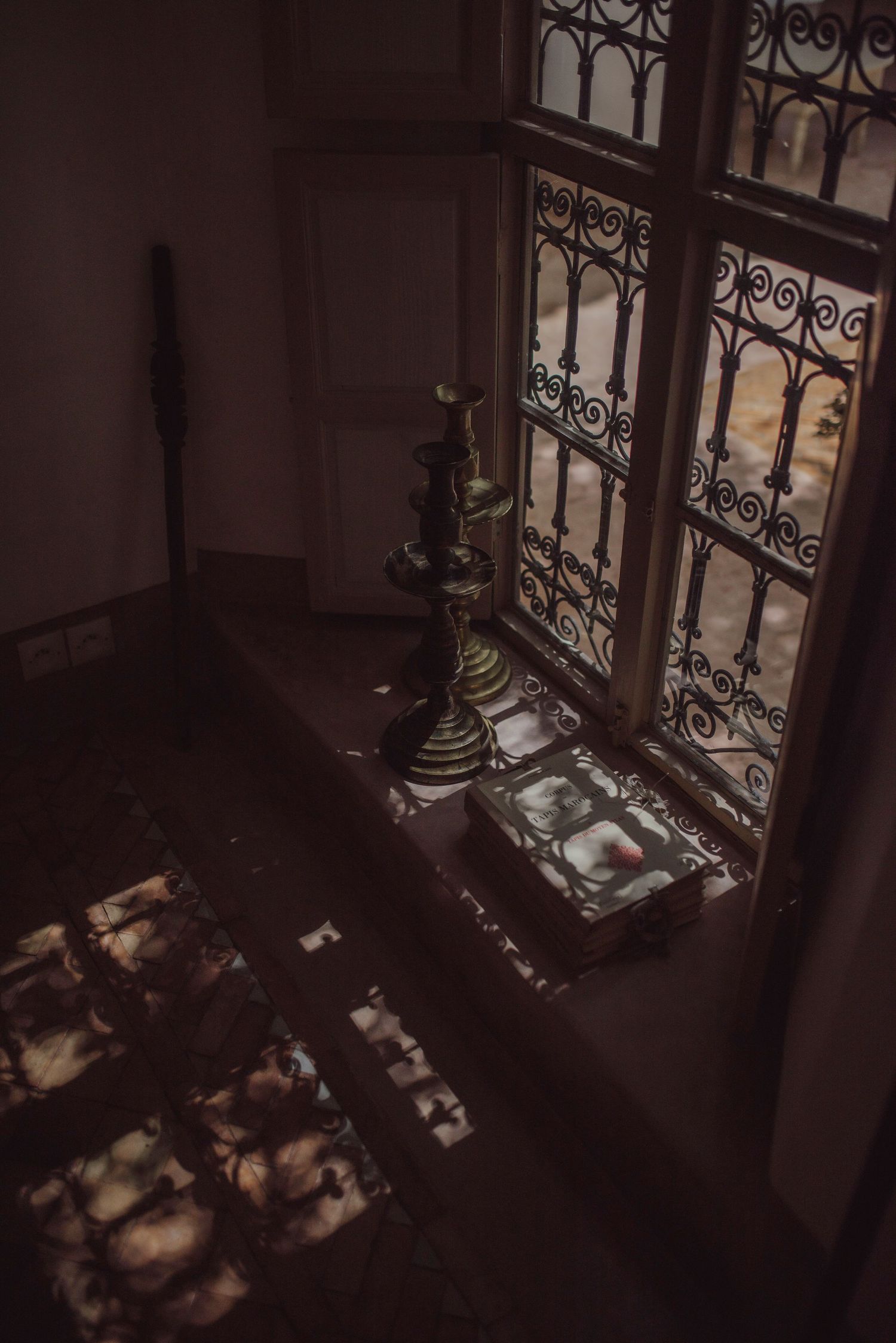 Ornate iron window with dramatic shadow patterns cast on dark interior floor.