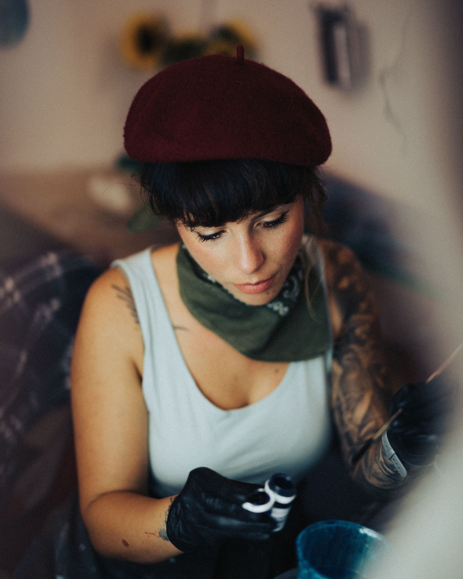 Person wearing a burgundy beret and white tank top concentrates while working with black gloves on.