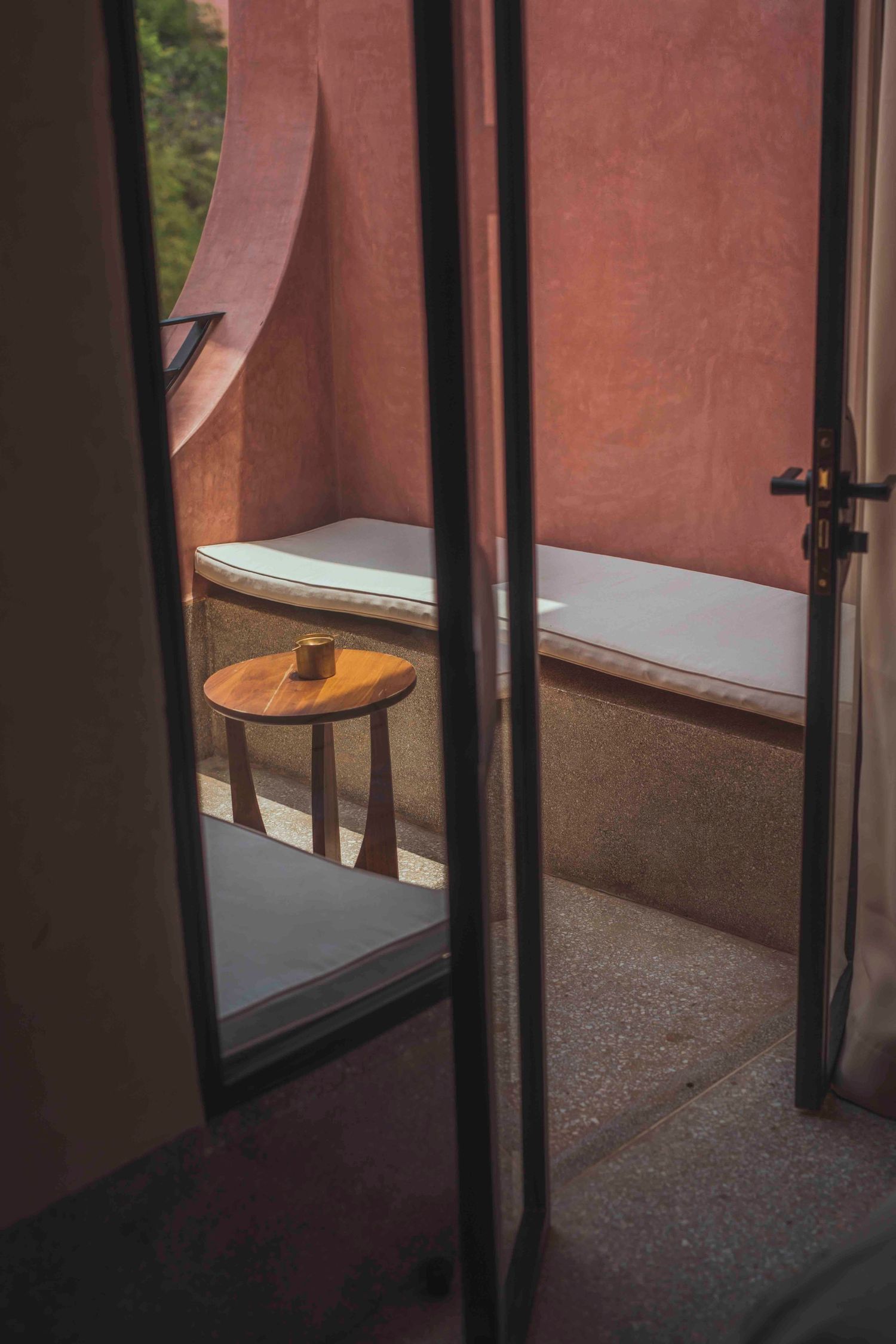 Wooden side table and cushioned bench seen through glass doors in modern interior.