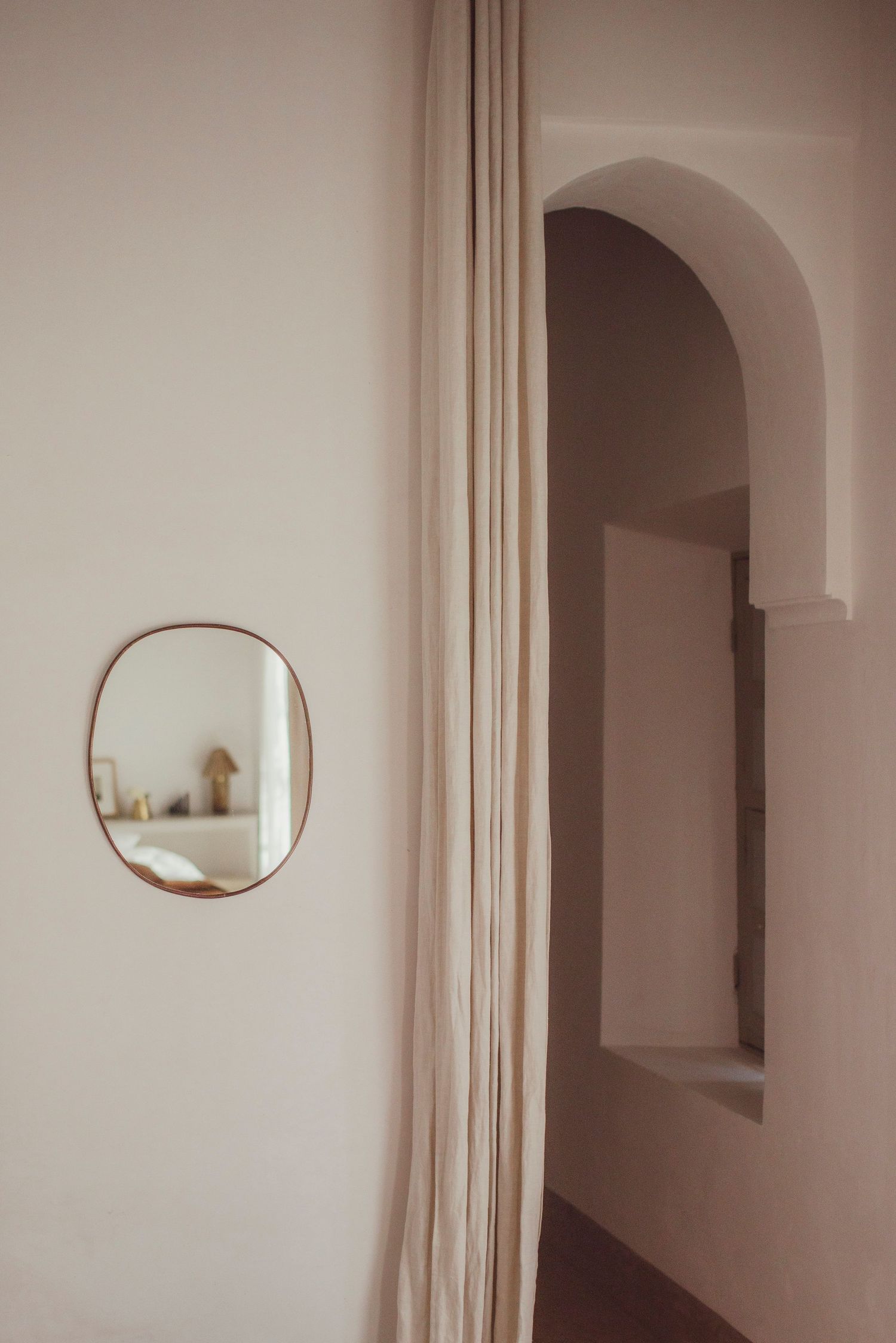 Minimalist interior hallway with arched doorway and round mirror on cream colored wall.