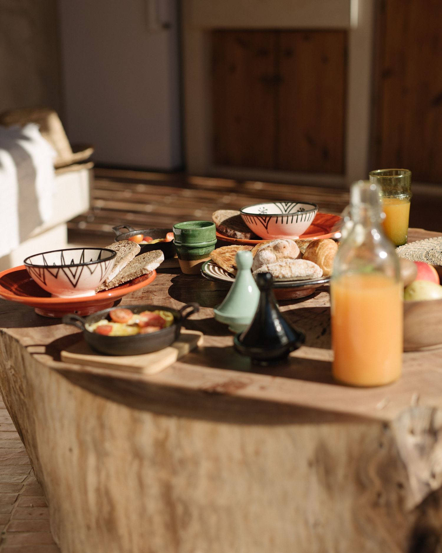 Rustic breakfast spread with orange juice, colorful dishes and pastries on a wooden table.