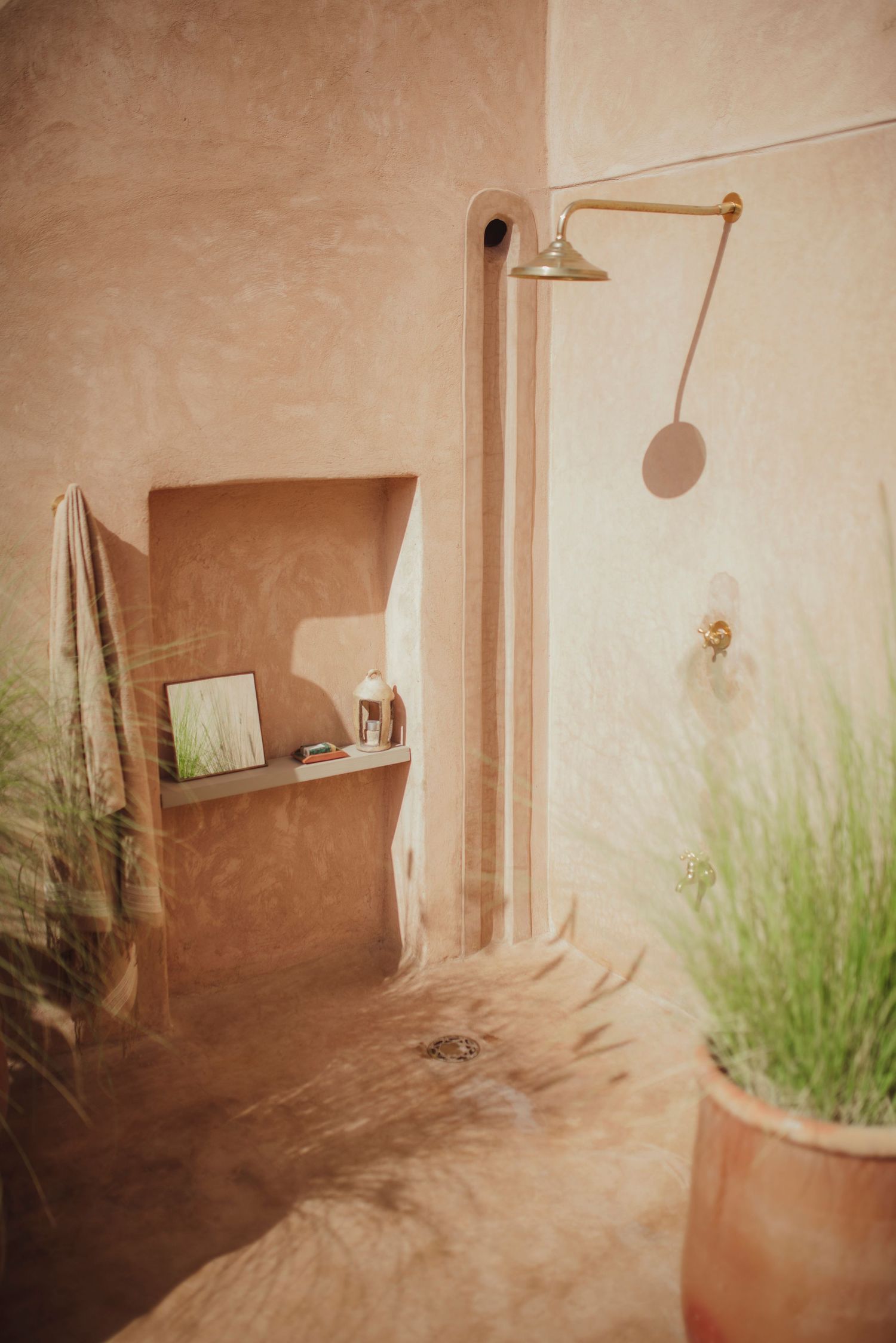 Modern bathroom interior with copper shower head and built-in shelf niche against textured walls.