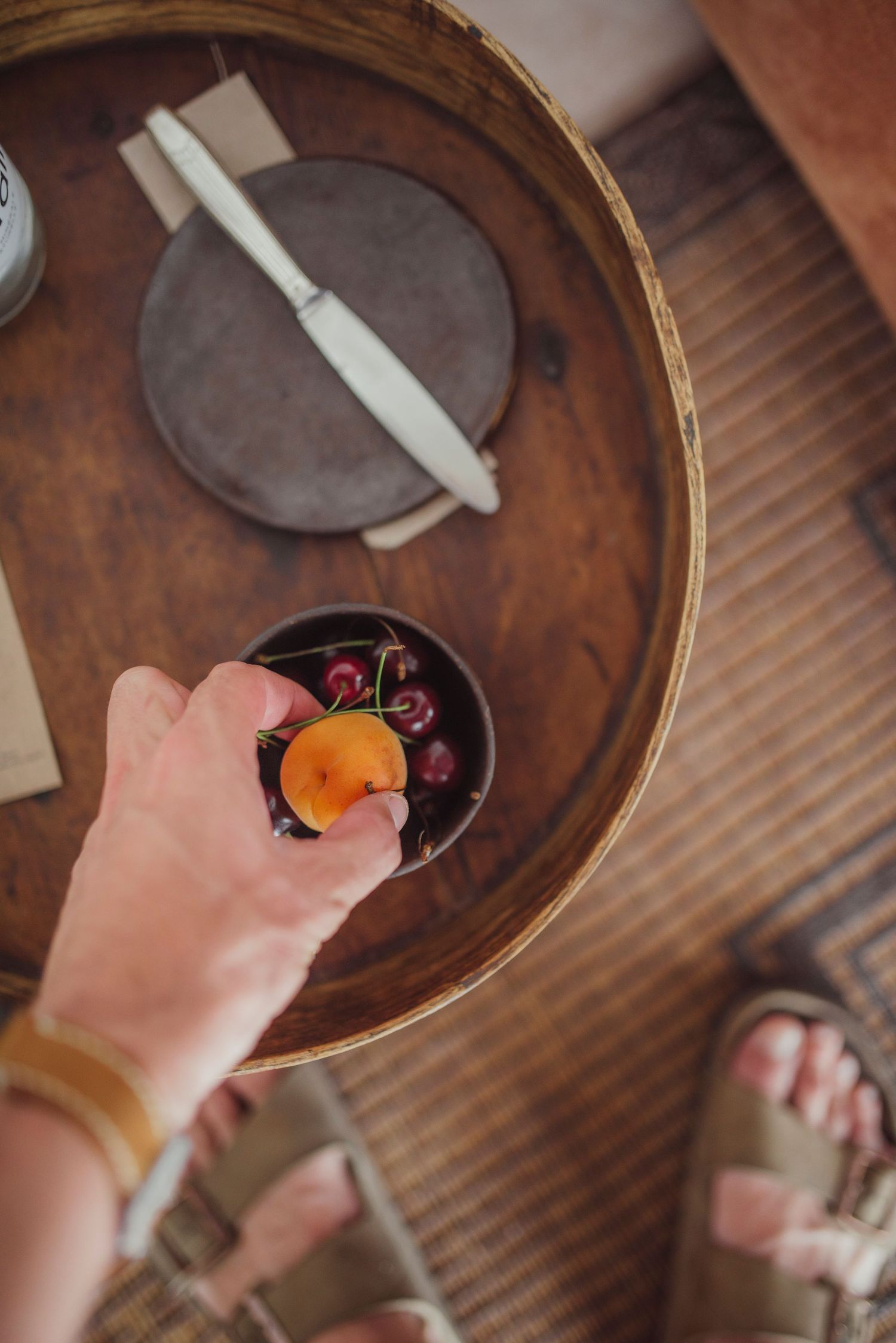 Overhead view of a hand reaching for a drink on a round wooden table.