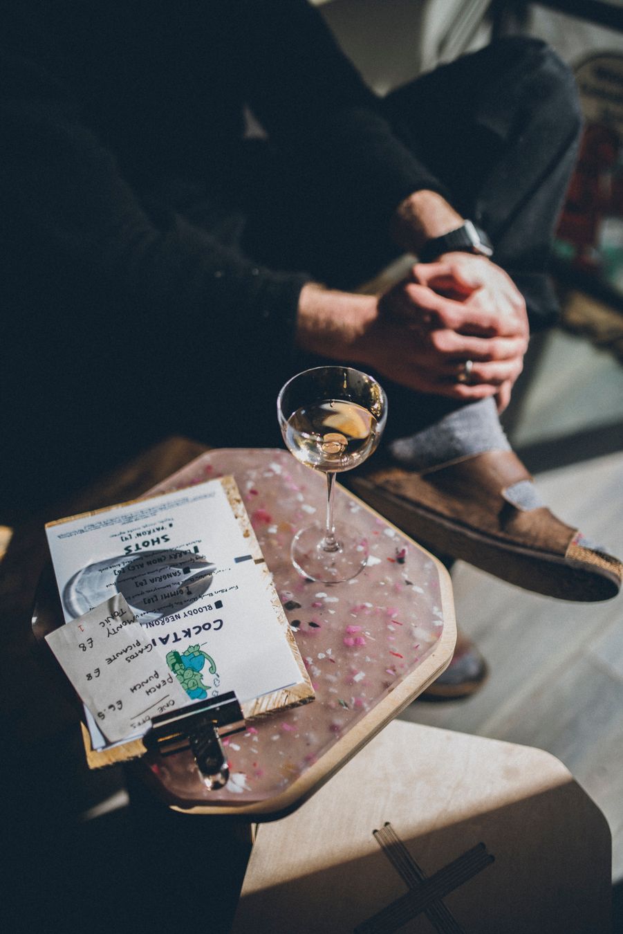 Martini glass and vintage records on wooden surface with person sitting nearby.