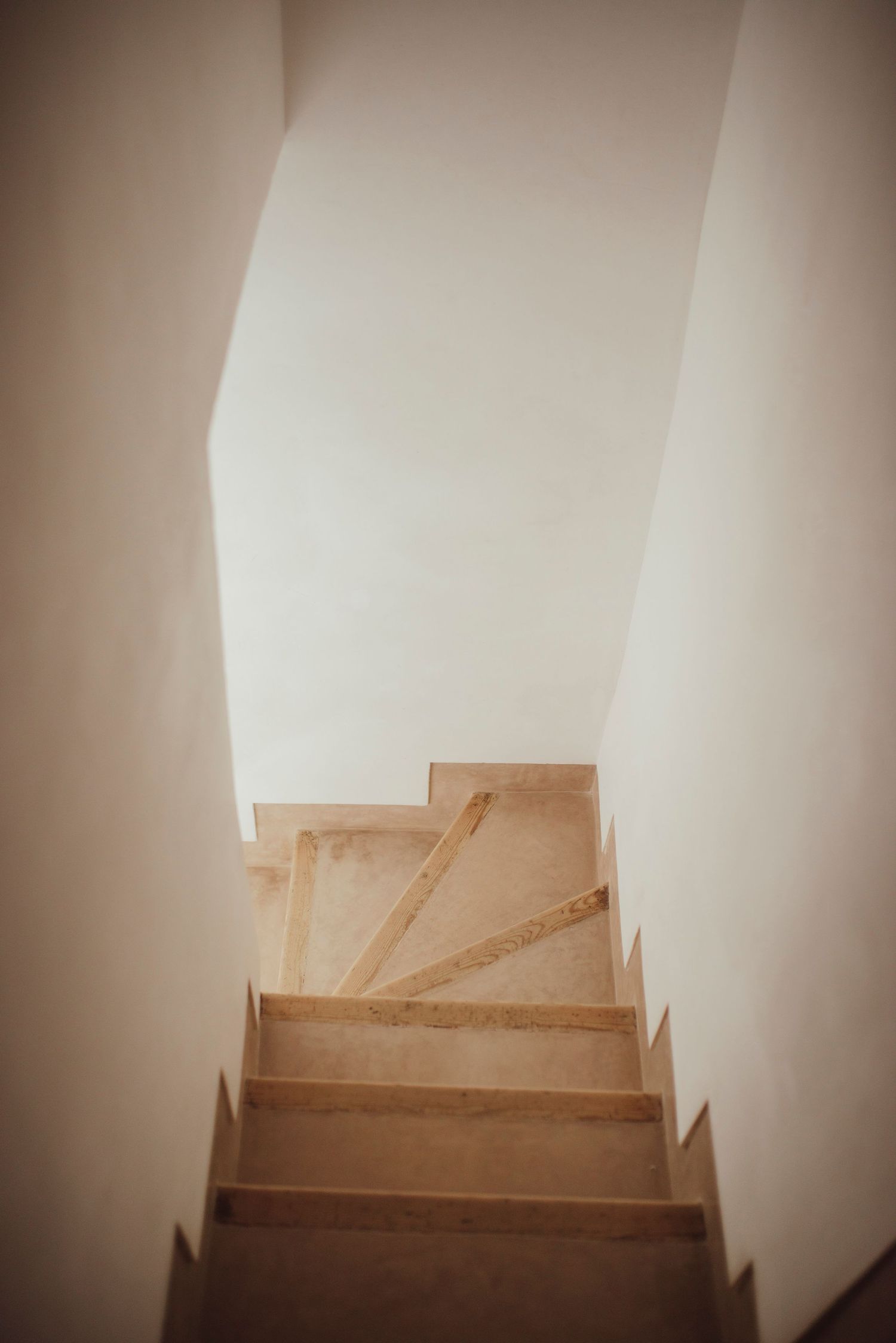 Minimalist staircase with white walls and wooden steps leading upwards in warm lighting.