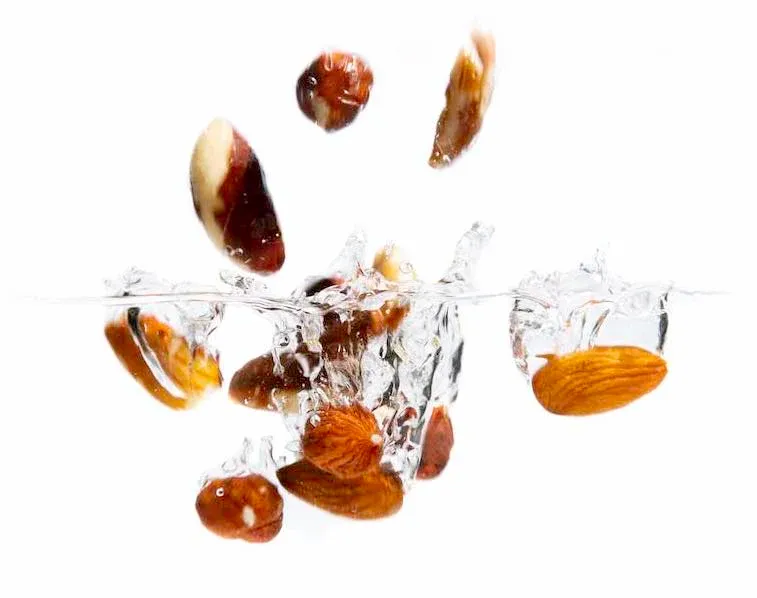 Nuts and dried fruits splashing into water with ice cubes creating dynamic ripples against white background.