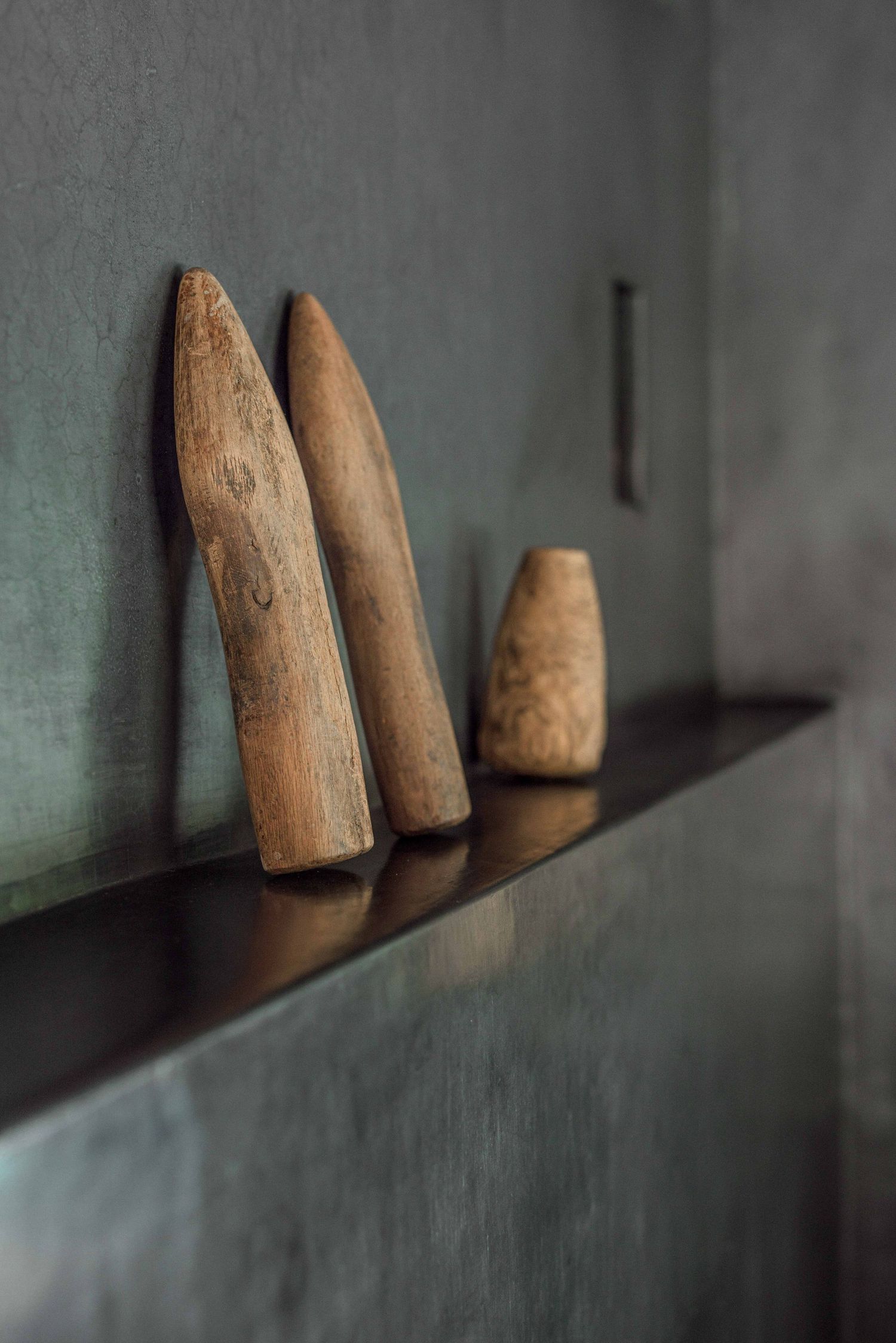 Wooden objects displayed in a row on a shelf create a minimalist composition against a soft gray background.