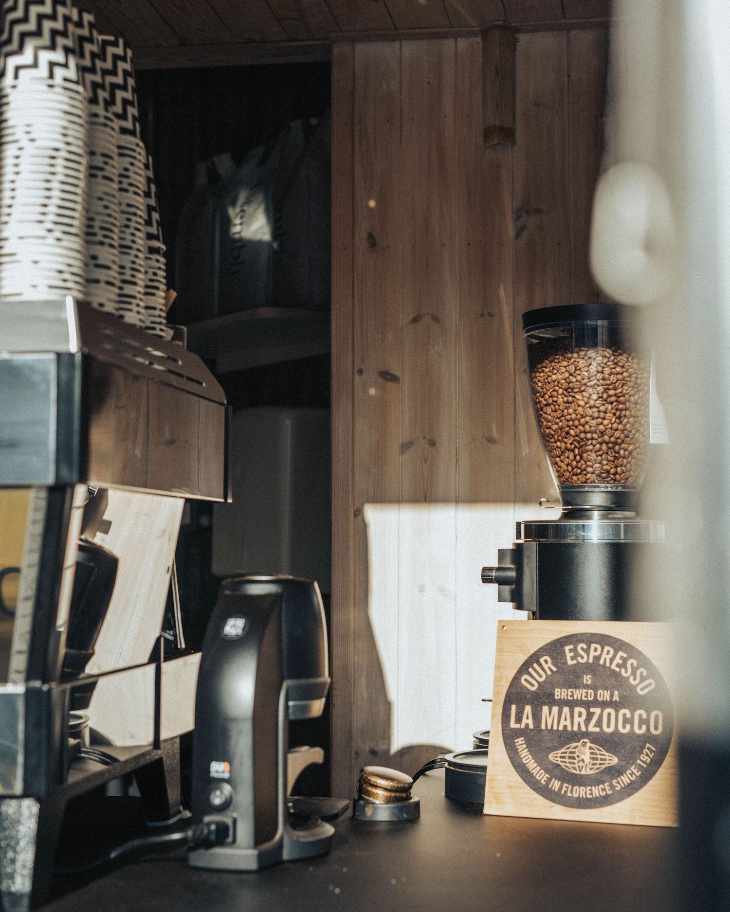 Coffee corner with vintage espresso equipment, grinder with coffee beans, and La Marzocco branded packaging on wooden shelf.