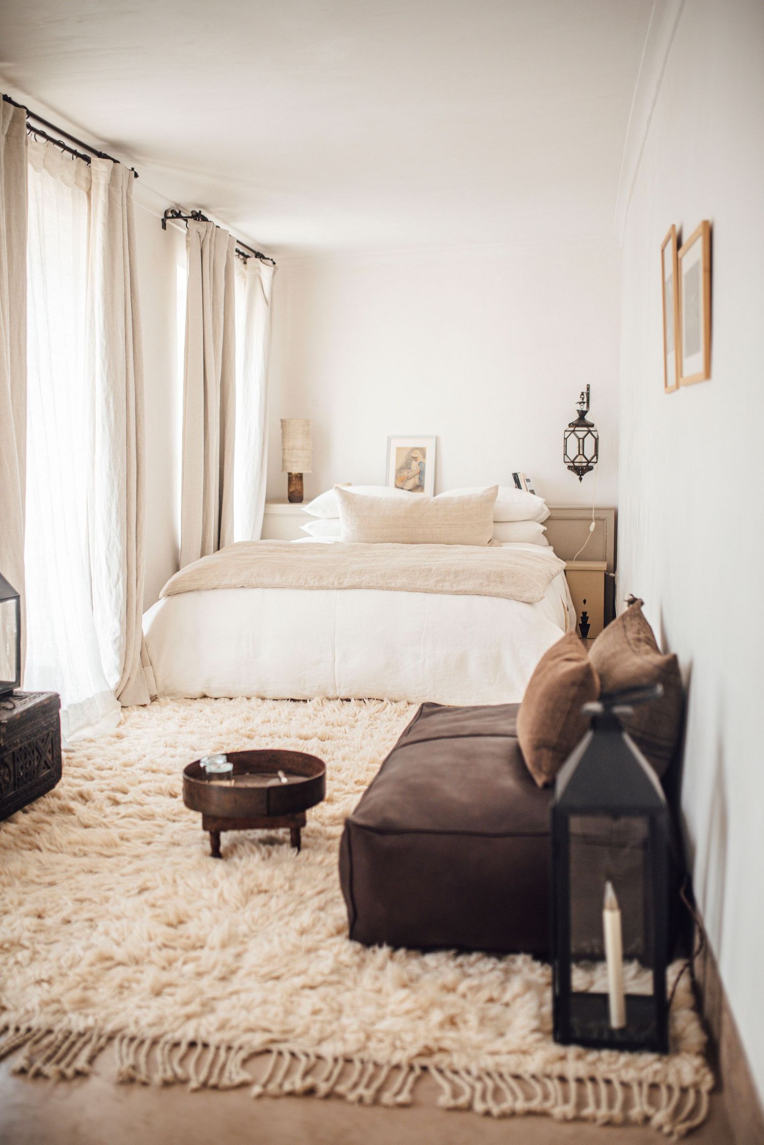 Minimalist bedroom with white bedding, shag rug, and natural curtains filtering light.
