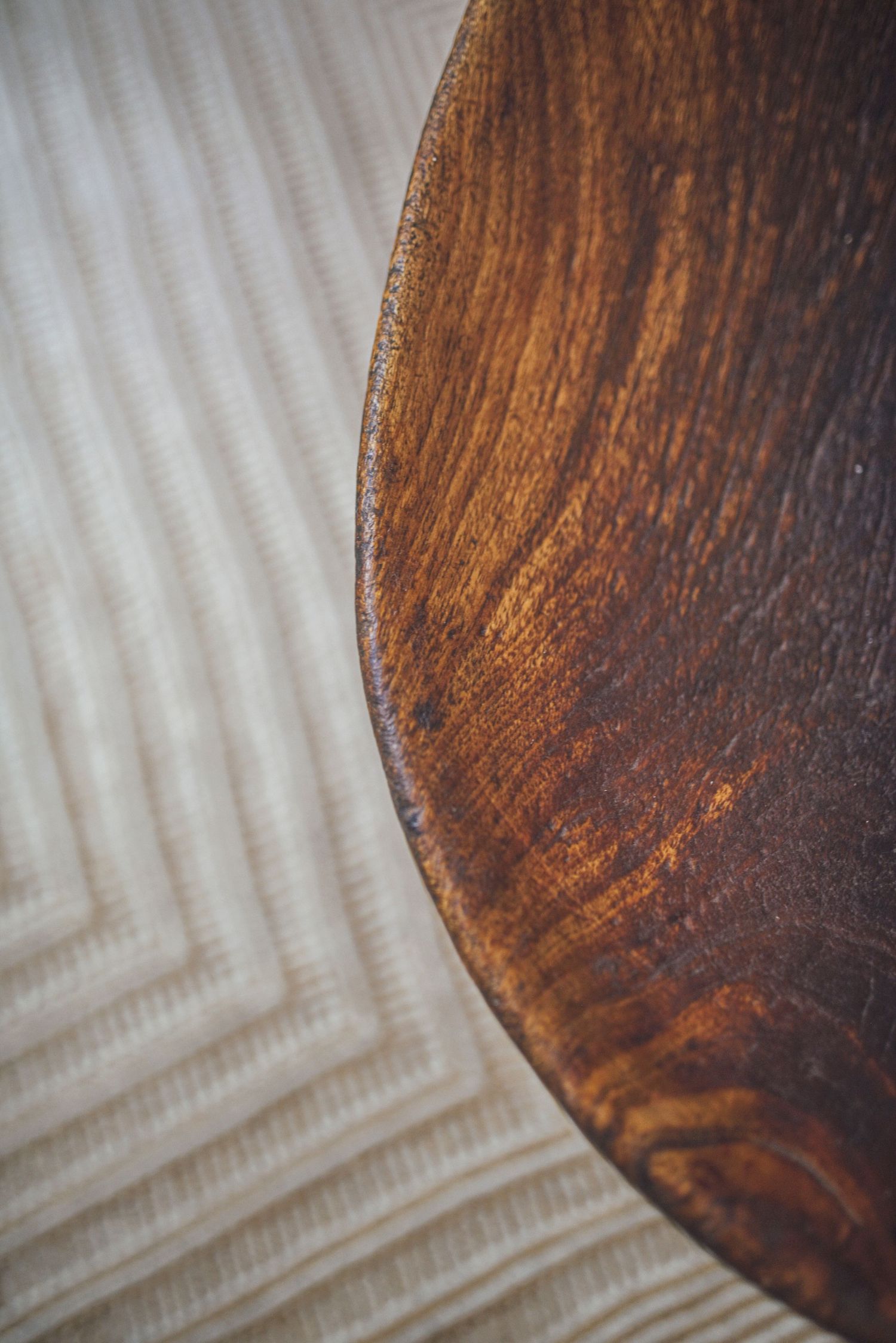 Close-up detail of a dark wooden surface with curved edge against a textured white background.