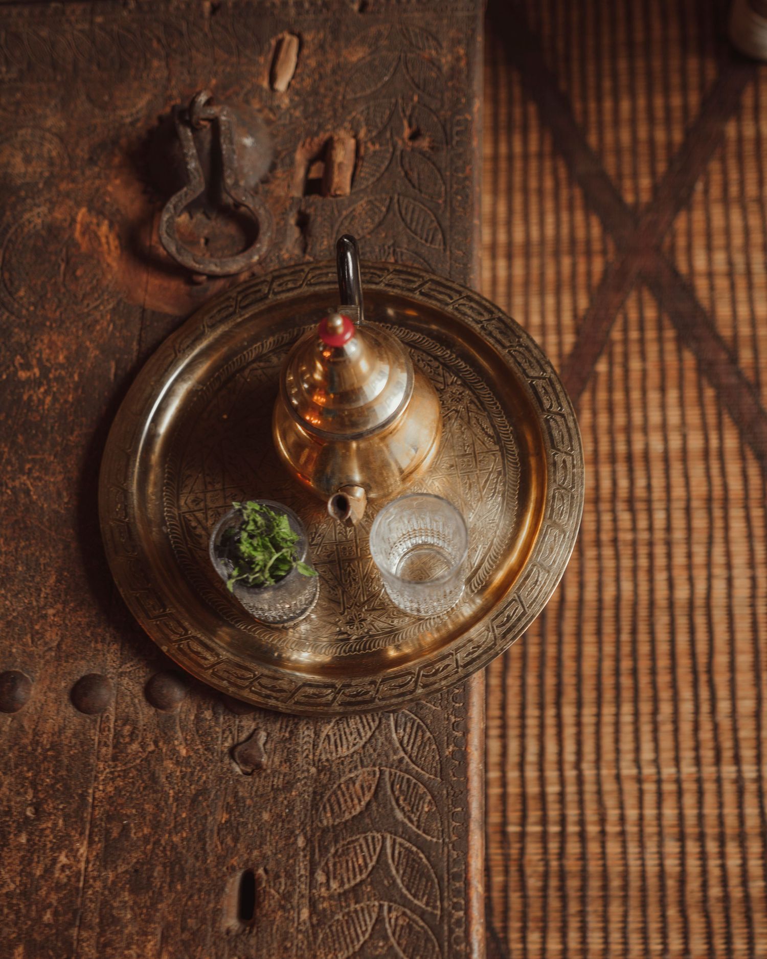 A brass teapot and glasses arranged on an ornate metal tray with shadow patterns.