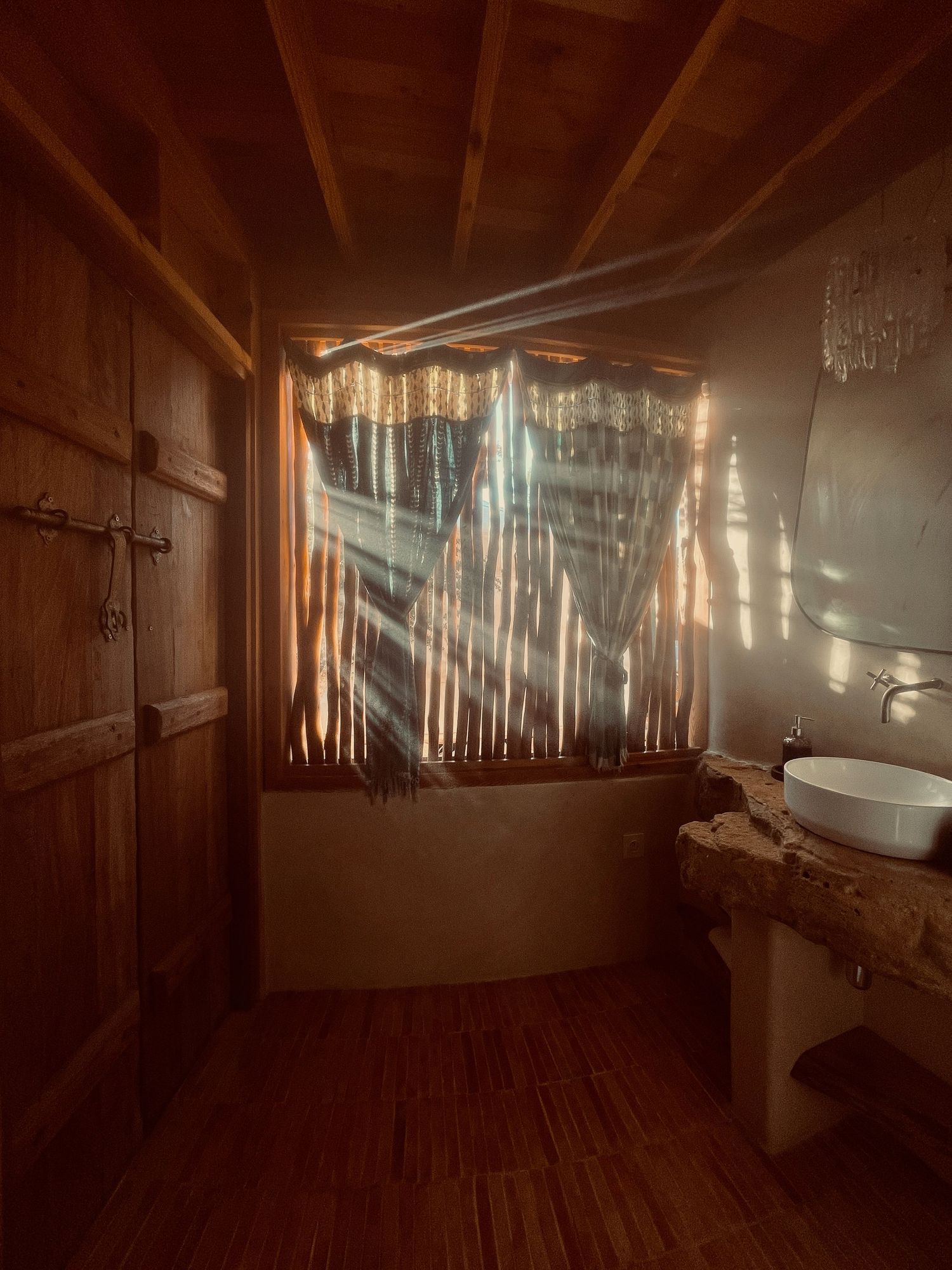 Sunlit bathroom interior with wooden walls and dramatic light beams streaming through window.