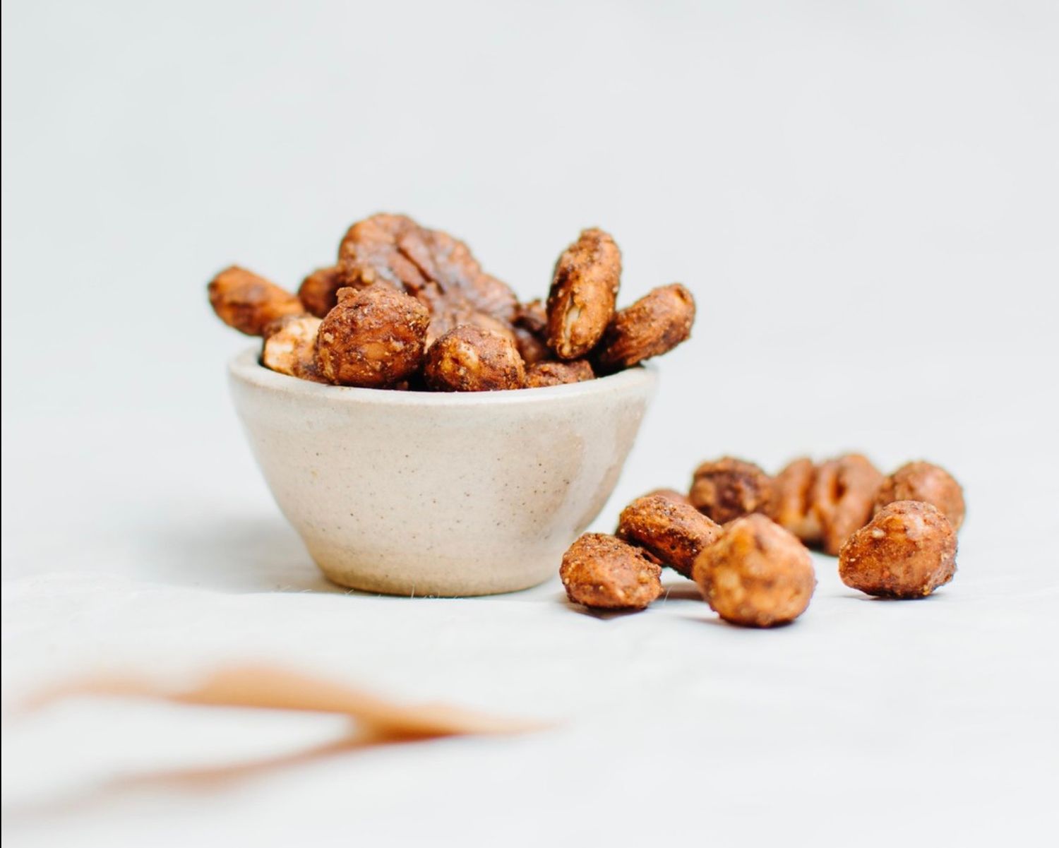 Editorial food photography of honey roasted cashews arranged on a white surface with small ceramic bowl.