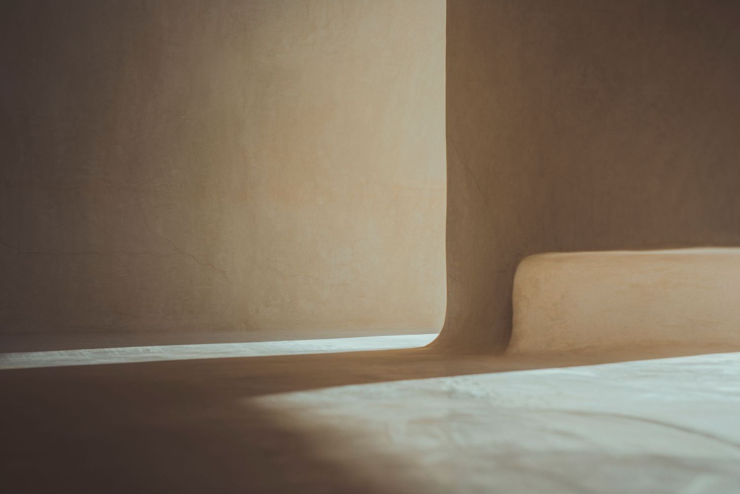 Sunlight casting geometric shadows on a minimalist beige wall and floor in an interior space.