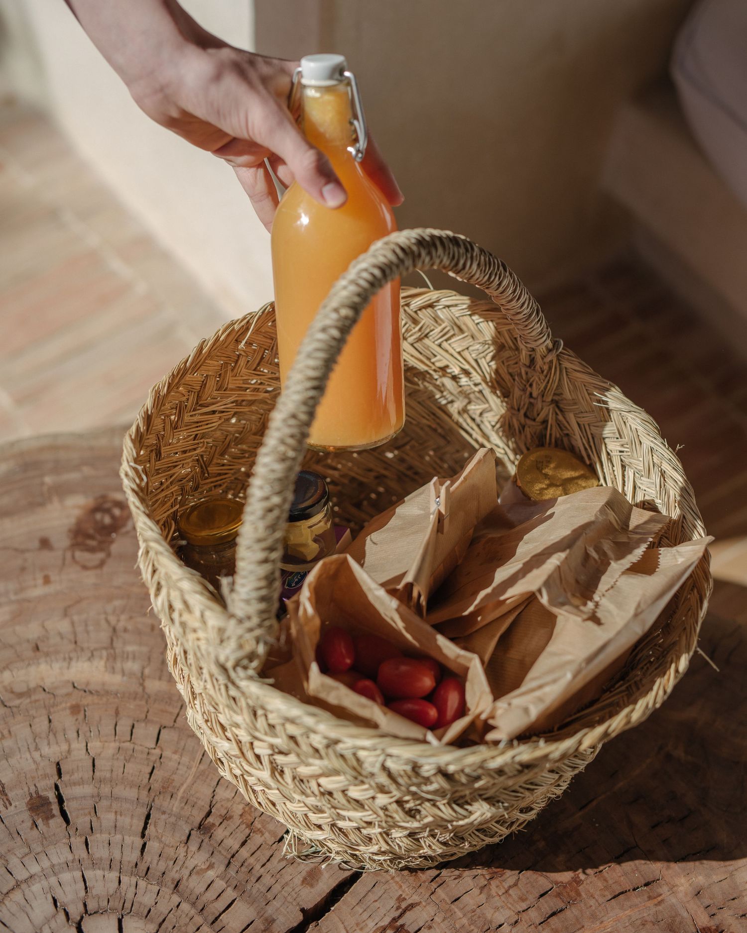 A woven basket containing a glass bottle of orange juice and paper-wrapped items on a wooden surface.