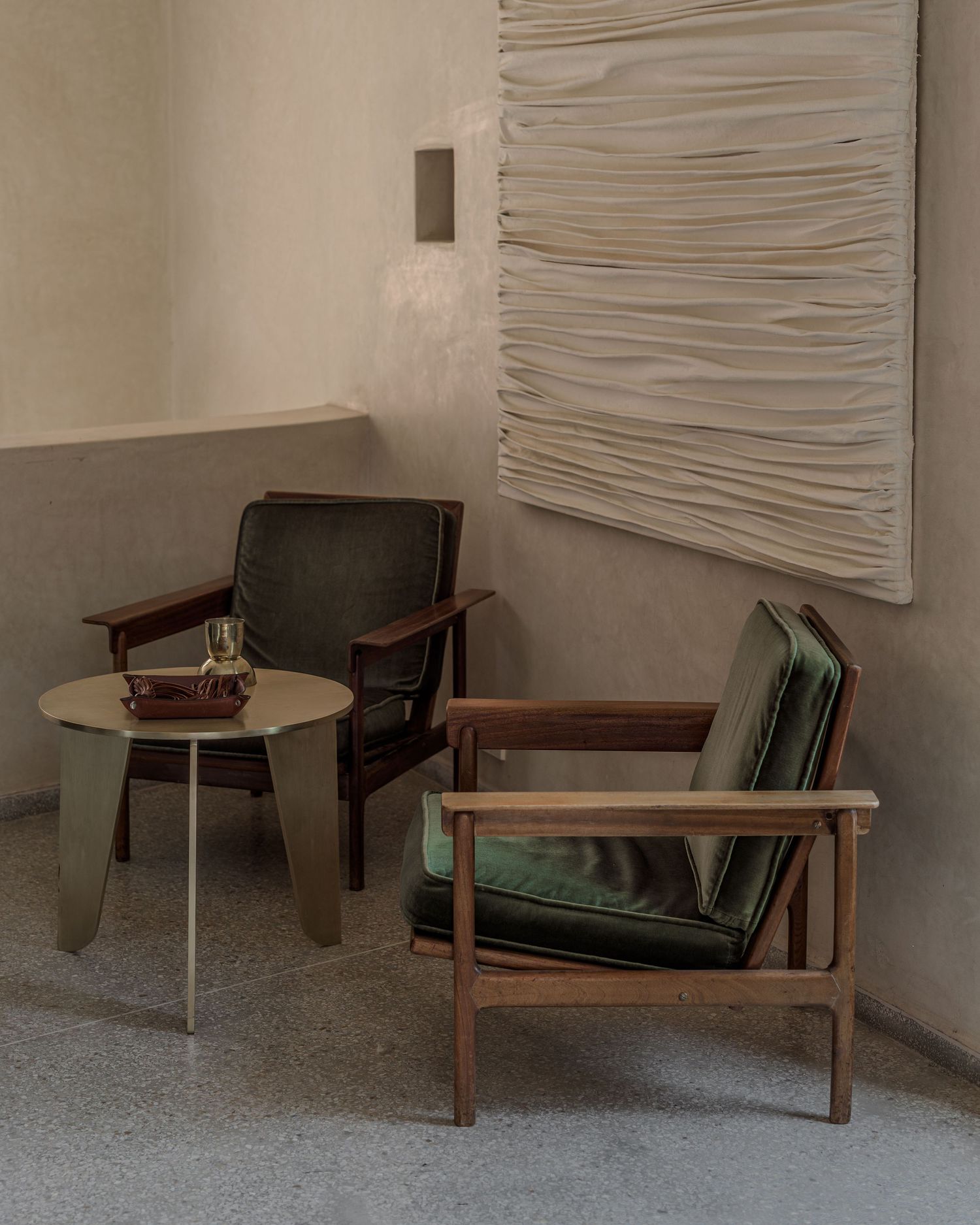Mid-century modern accent chair with green cushions against textured white wall in minimalist interior setting.