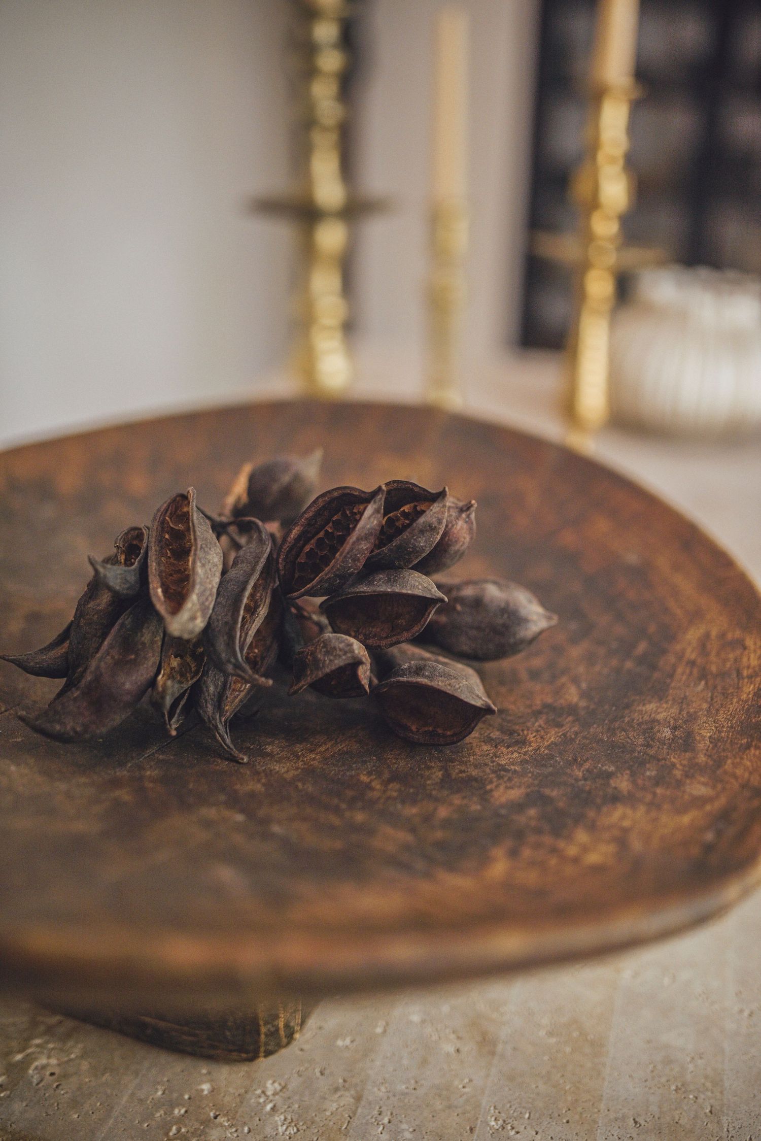 Dried pine cone on rustic wooden plate with golden candlesticks in background.