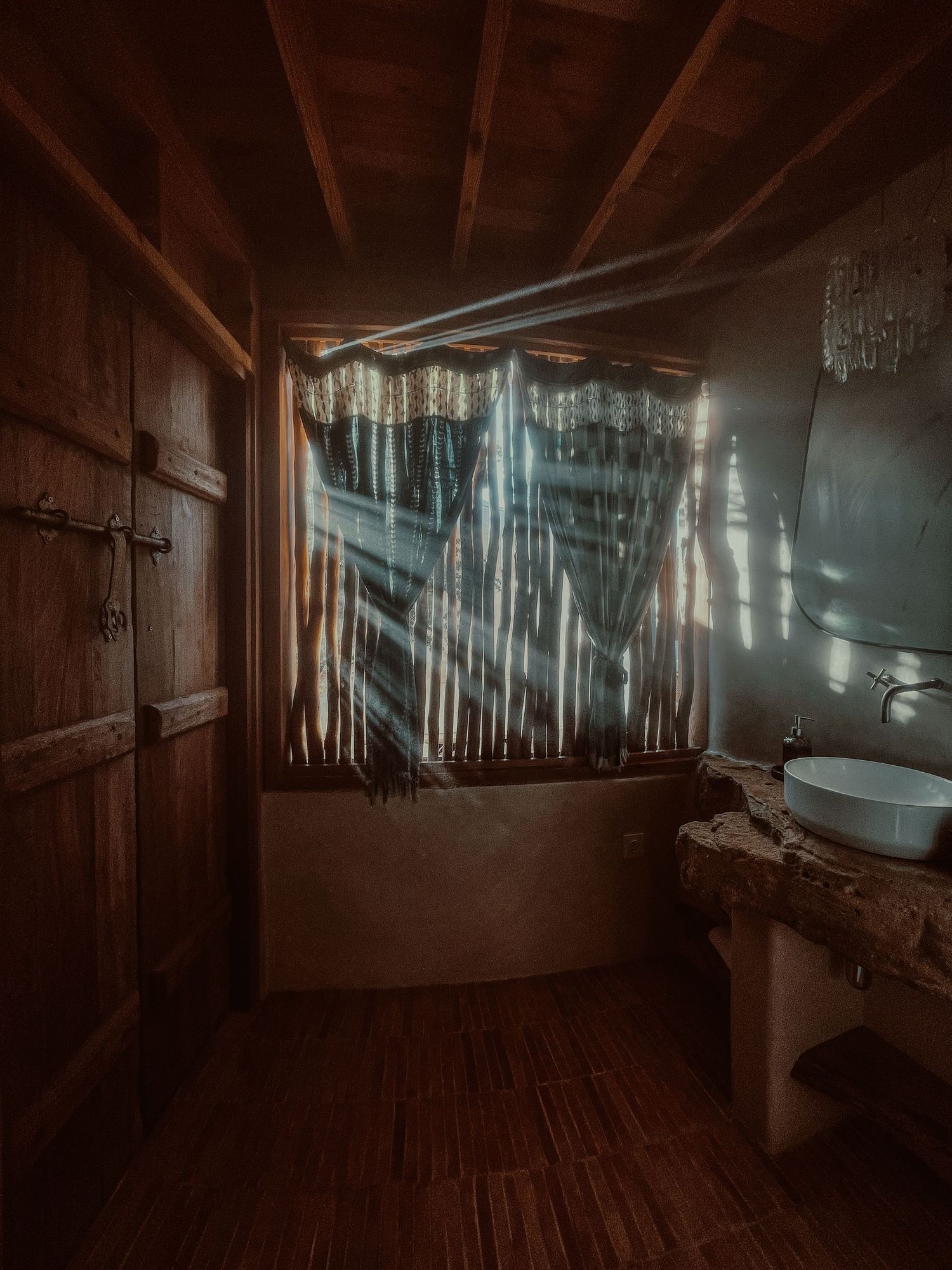 Light rays filtering through curtains in a dark wooden bathroom creating ethereal patterns.