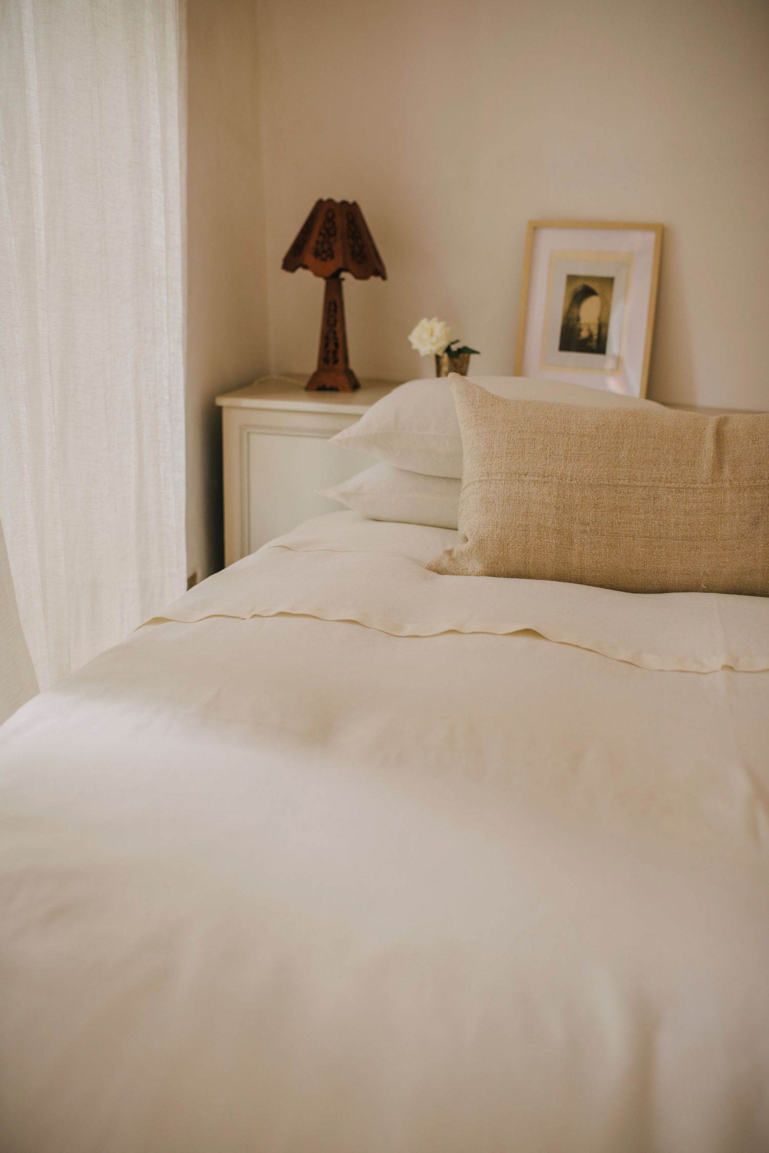 Cozy bedroom corner with white bedding, decorative lamp, and framed artwork.