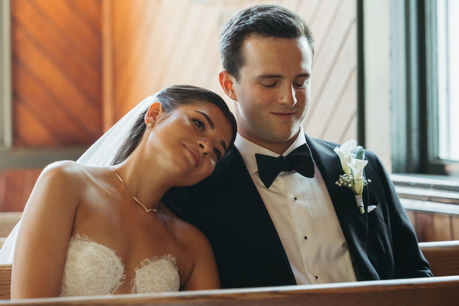 Elegant wedding couple sharing a tender moment in formal attire by a window.