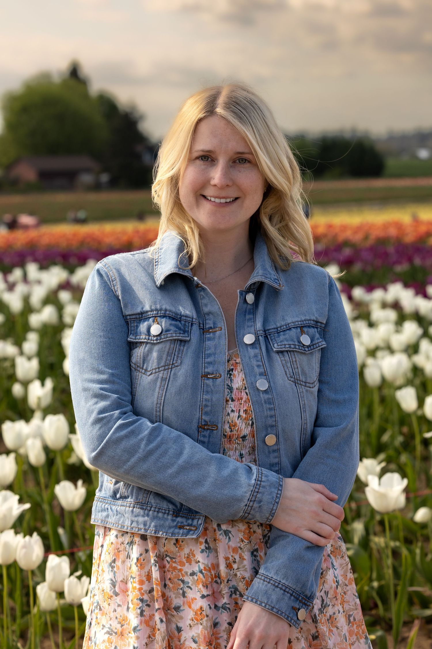 Someone wearing denim jacket poses in field of white and colorful tulips during golden hour.