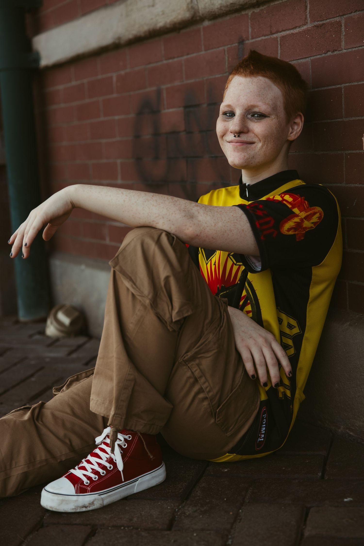 Person wearing brown pants and red sneakers posing casually against brick wall.