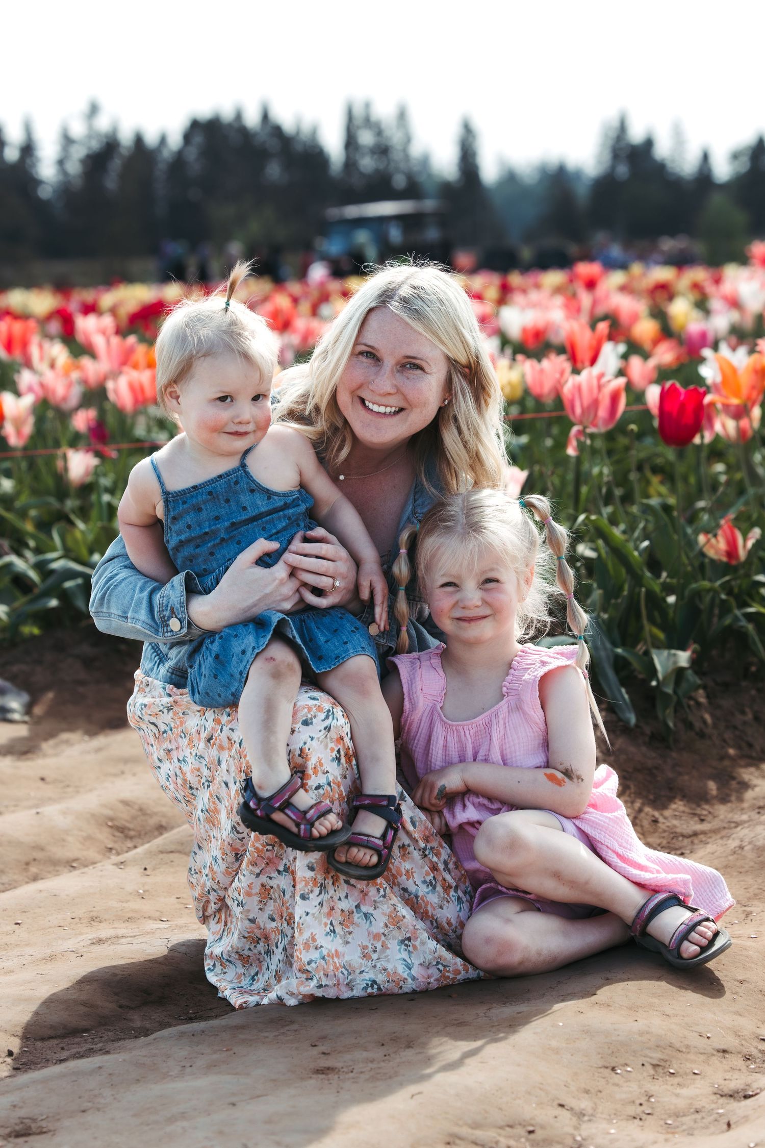 Three people share a tender moment among colorful tulip fields on a sunny day.