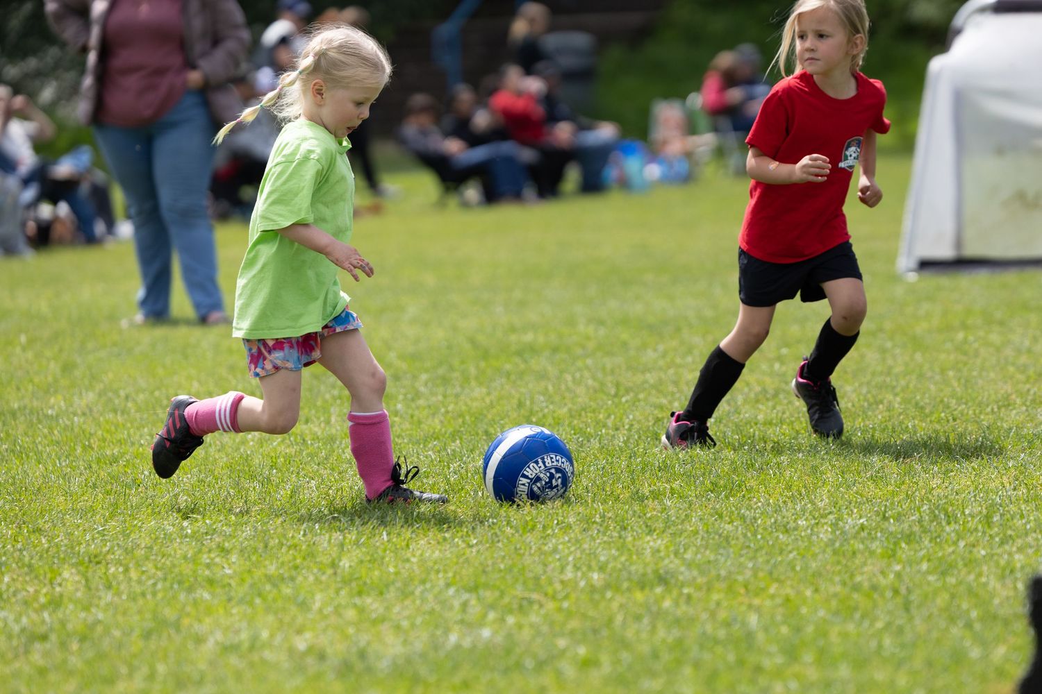 Young soccer players in bright jerseys compete for the ball during a youth match on a sunny grass field.