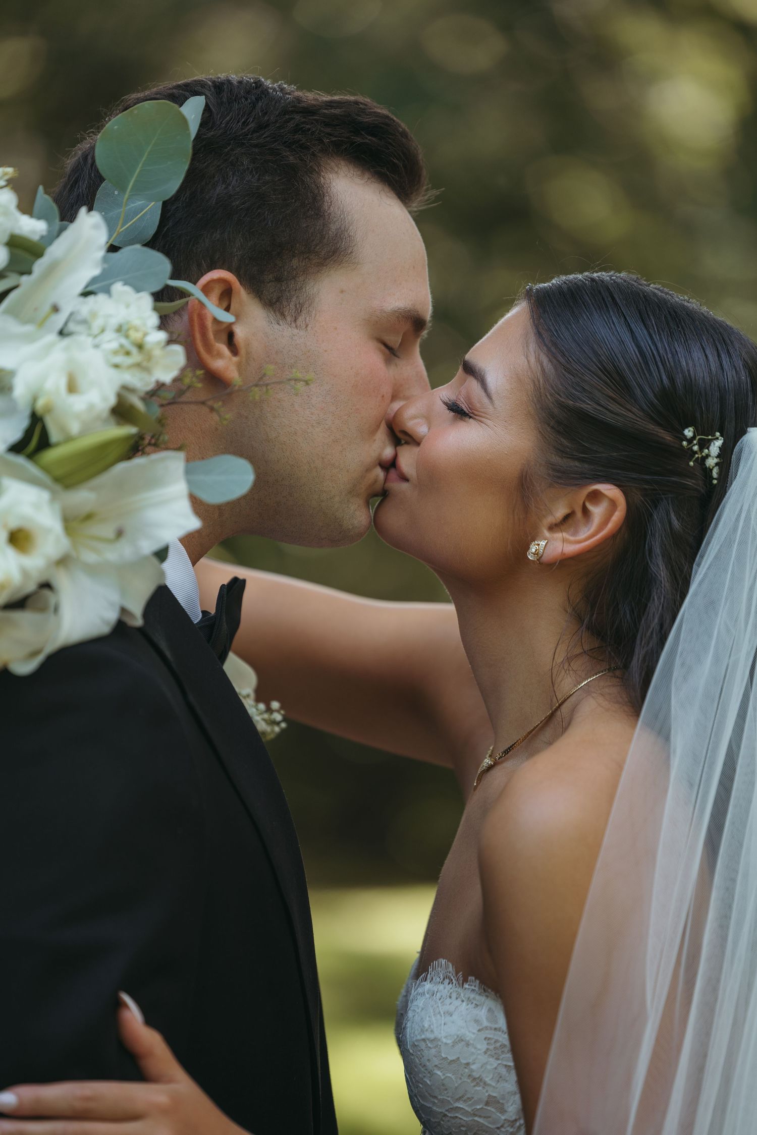 Newlyweds share romantic kiss with white flowers in outdoor setting.