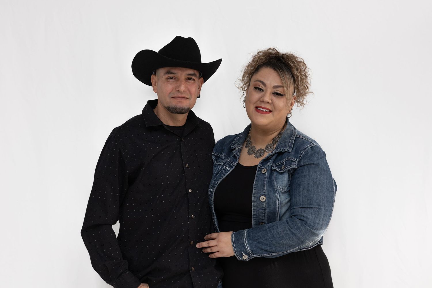 Stylish couple in western wear posing against white background.