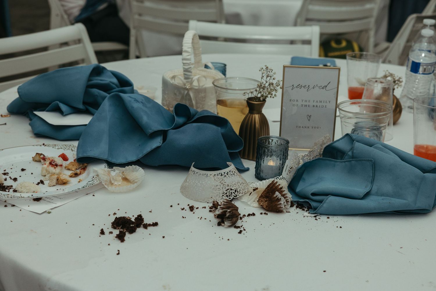 Reception table with blue napkins and scattered dessert remains after wedding celebration.