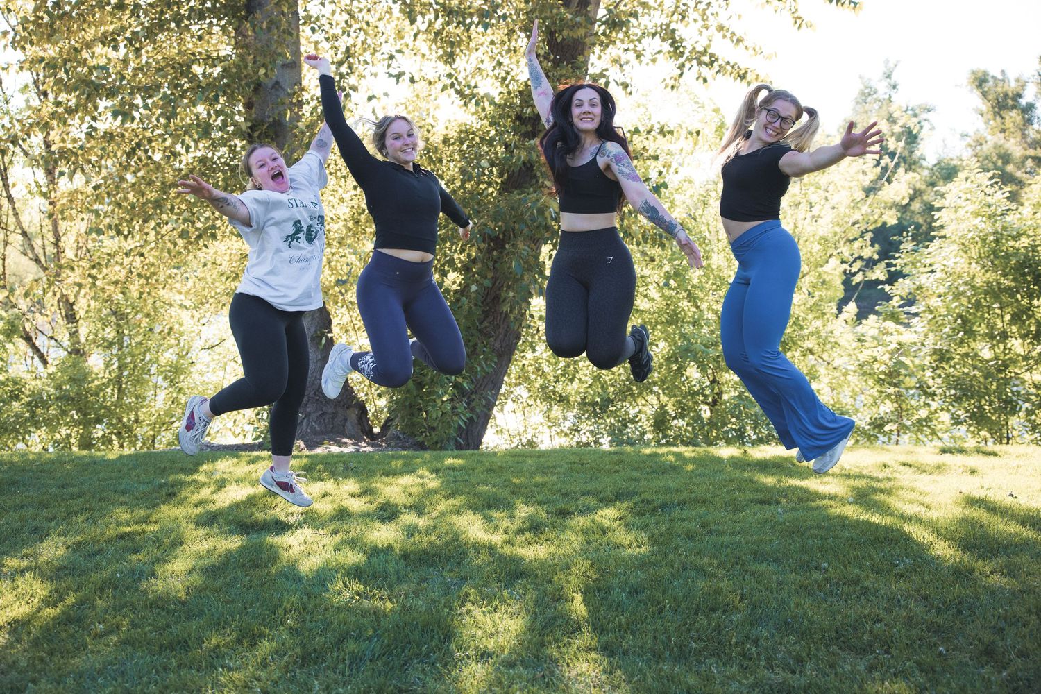 Group of people jumping joyfully in a line on a grassy hill during a sunny outdoor photo session.