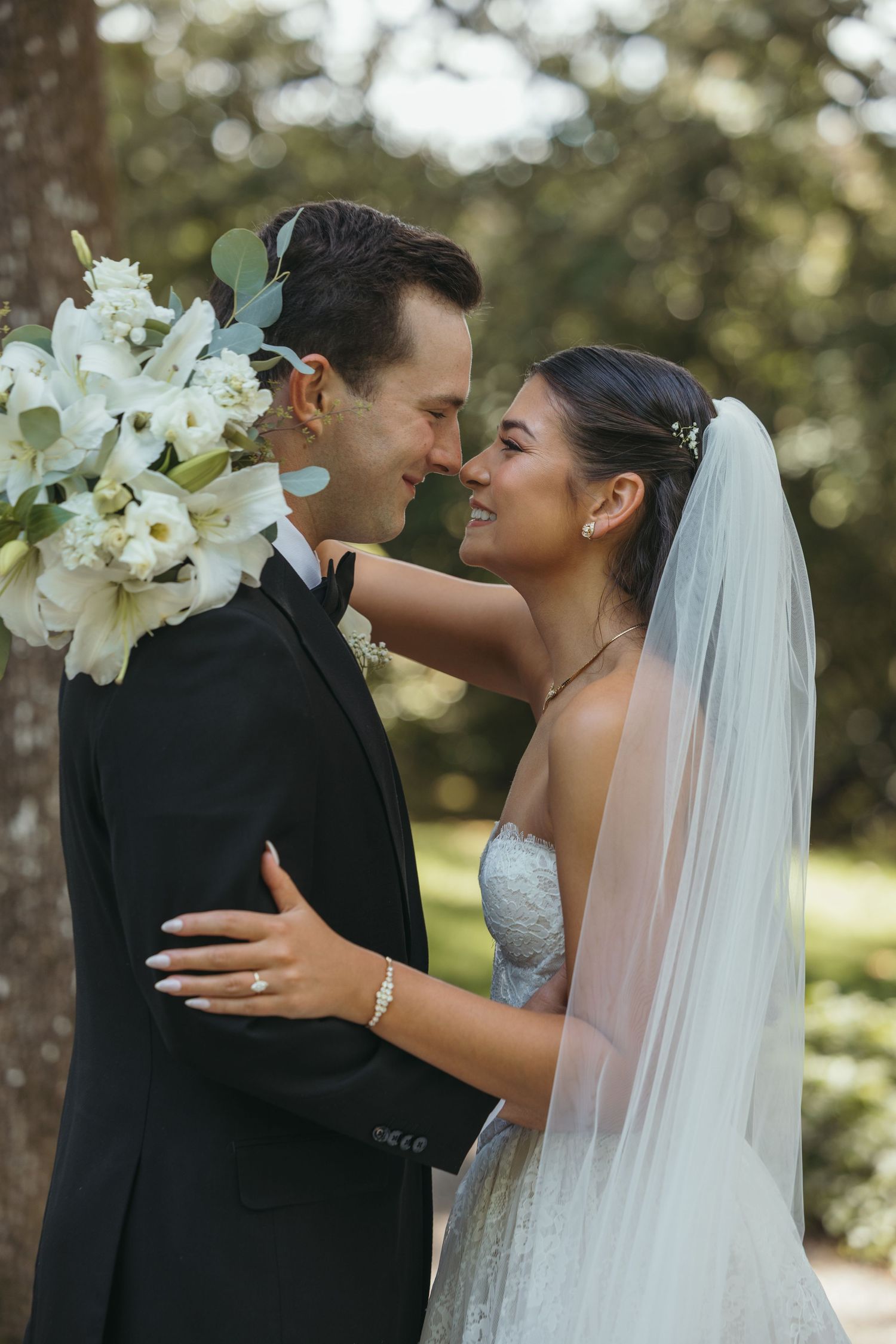 Elegant wedding couple shares intimate moments with white lilies and flowing veil.