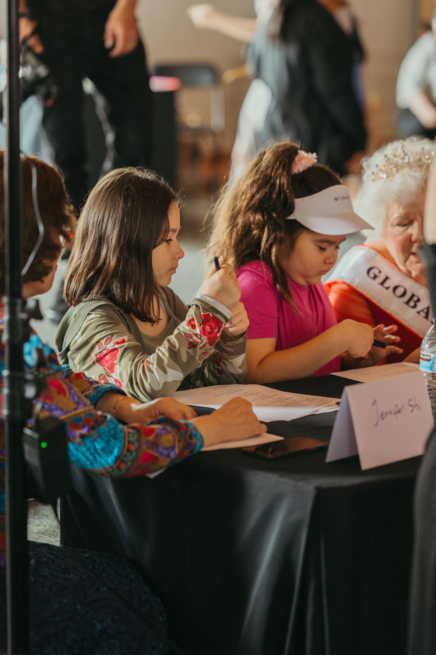 Children sitting at registration table during event with papers and drinks.