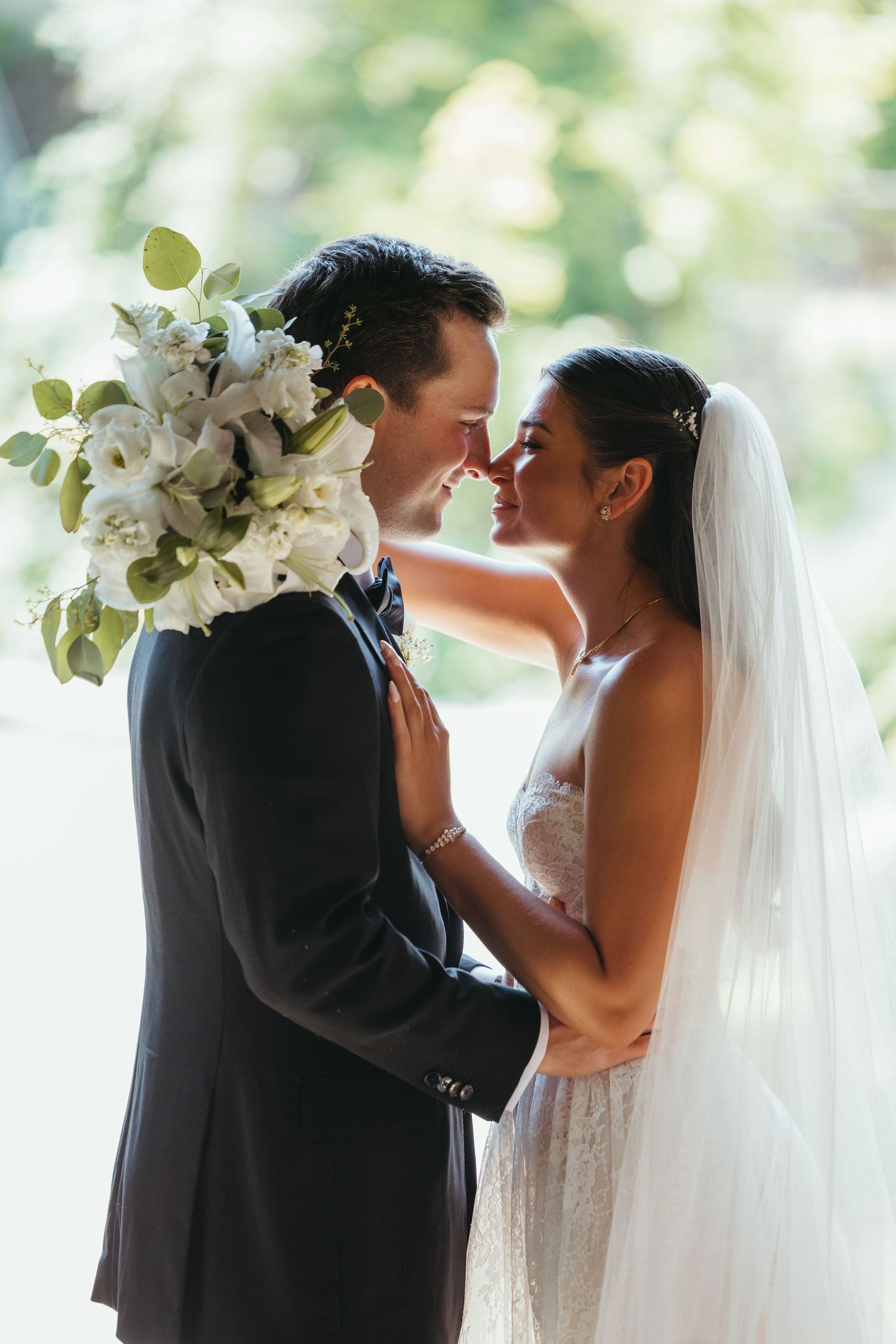 Romantic wedding couple shares intimate moment with white floral bouquet.
