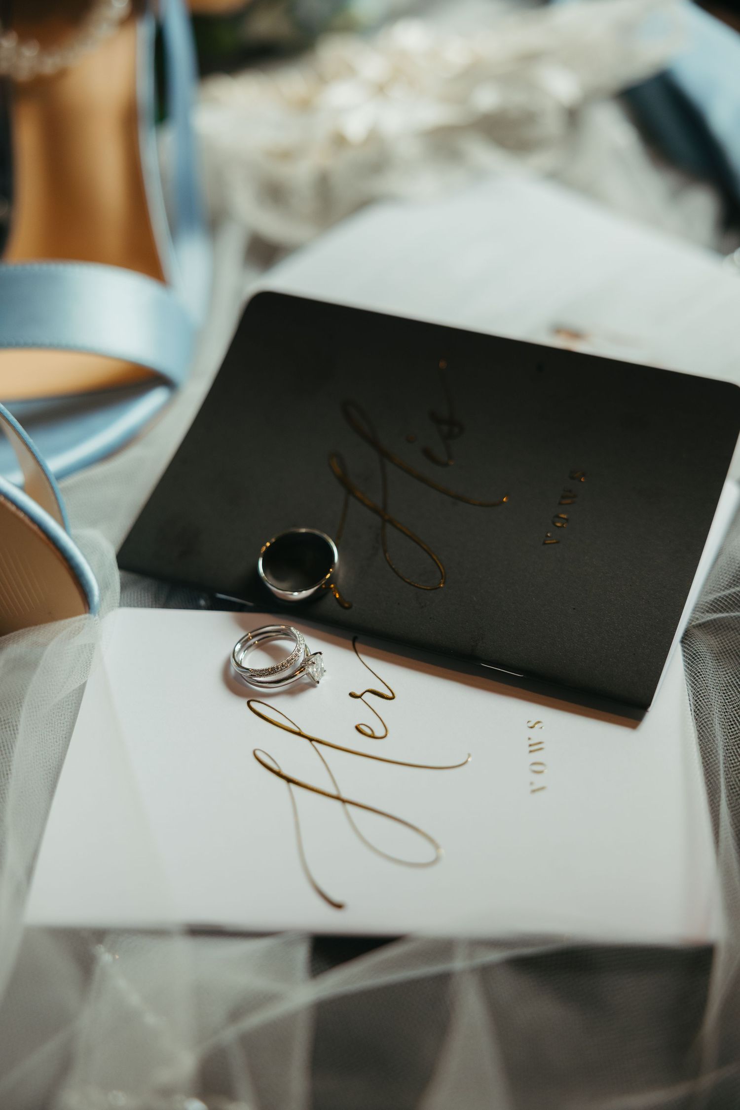 Wedding vows books in black and white with wedding rings resting on delicate tulle fabric.