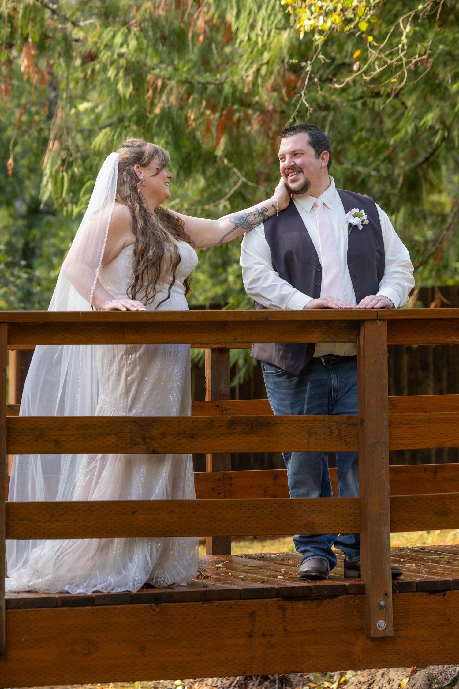 A bride and groom share a joyful moment together on a wooden bridge surrounded by lush greenery.