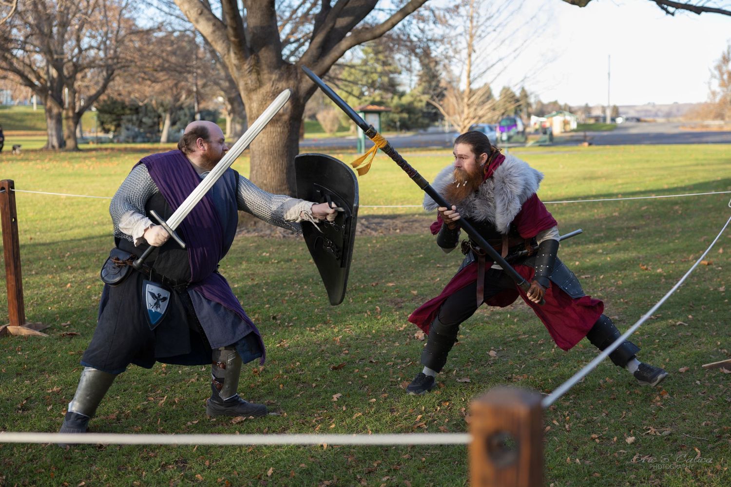 Medieval combat reenactors demonstrate sword fighting techniques in an outdoor setting.