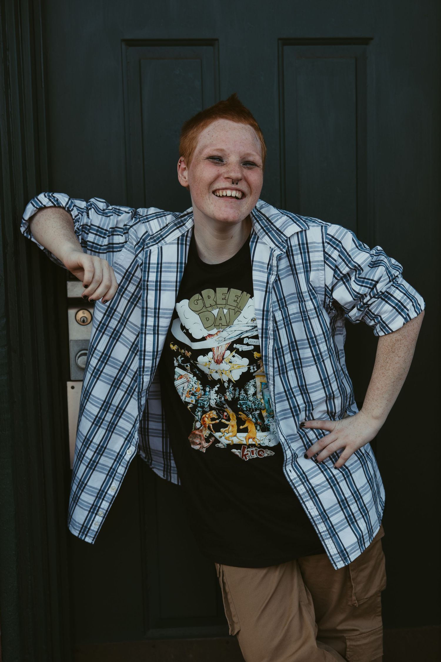 Person in plaid shirt and graphic tee showing playful poses against dark background.
