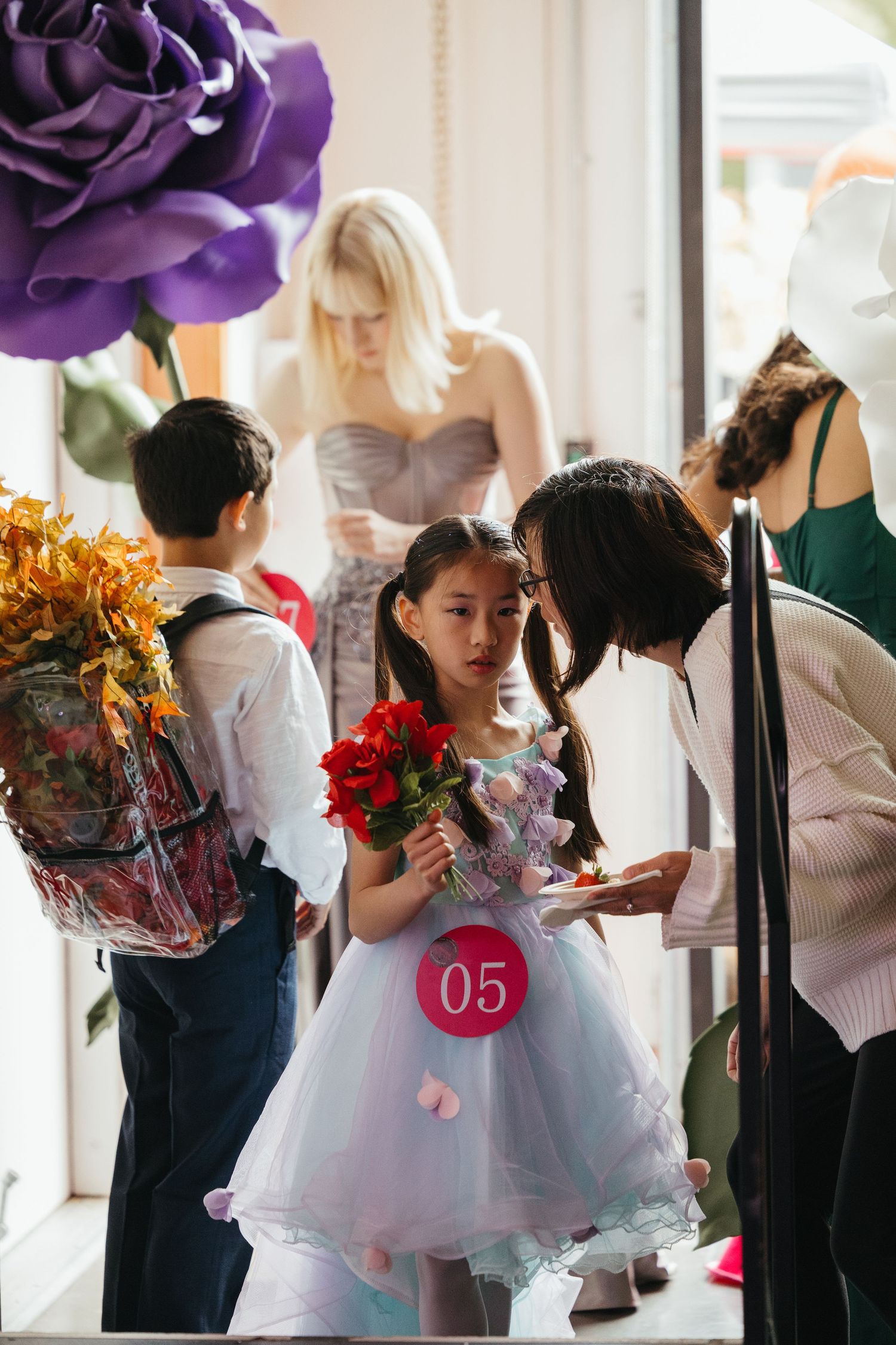 Elegant figures in formal attire gather at an event with purple floral decorations.
