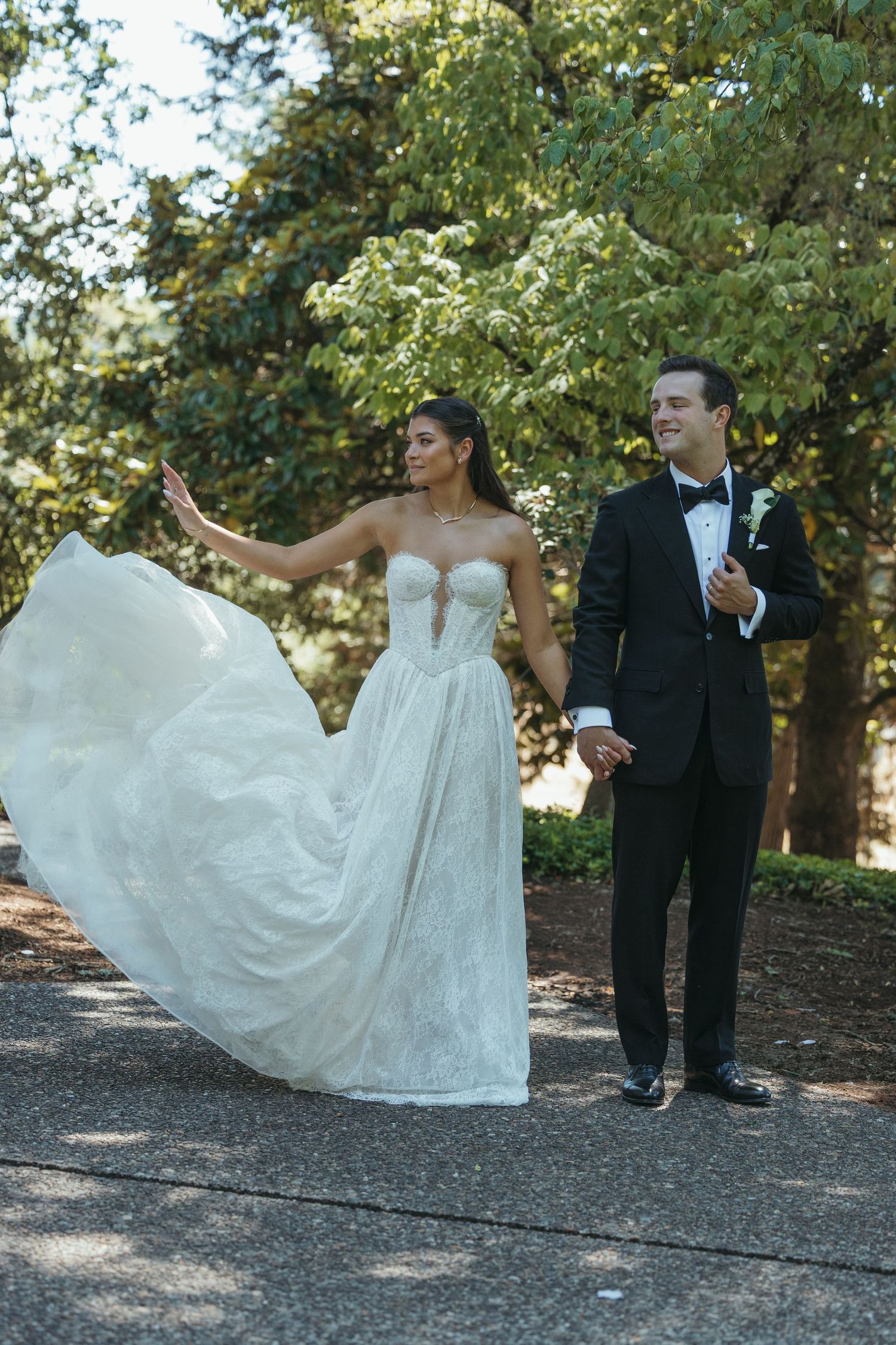 A couple poses outdoors on their wedding day with the bride's white dress flowing in the breeze.
