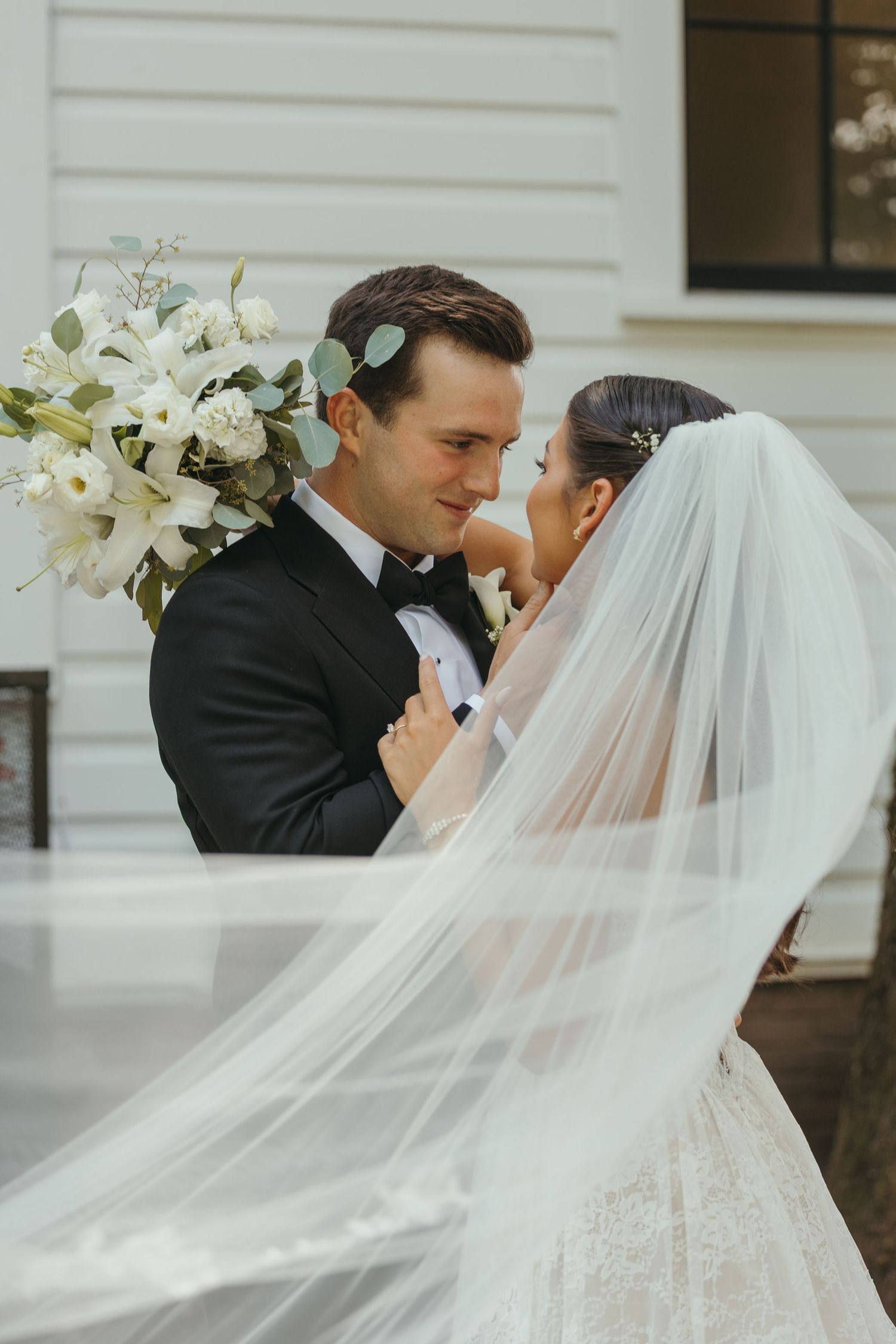 An elegant bride and groom share an intimate moment with white lilies and a flowing veil.